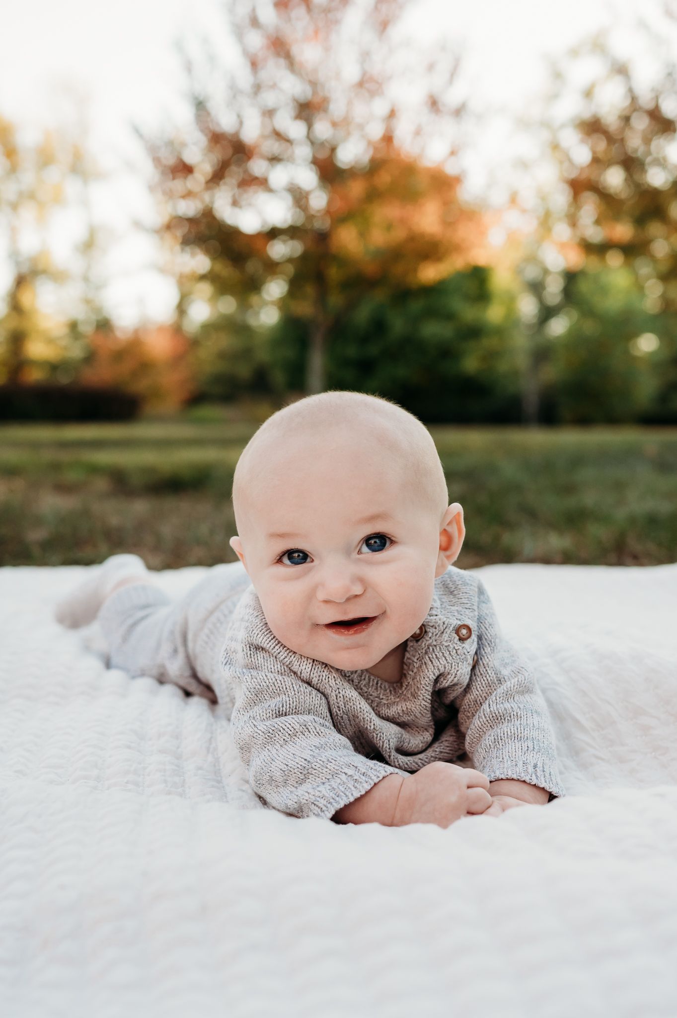 A baby lies on a white blanket outdoors in Plainfield, Indiana, during an autumn photo session with grandparents.