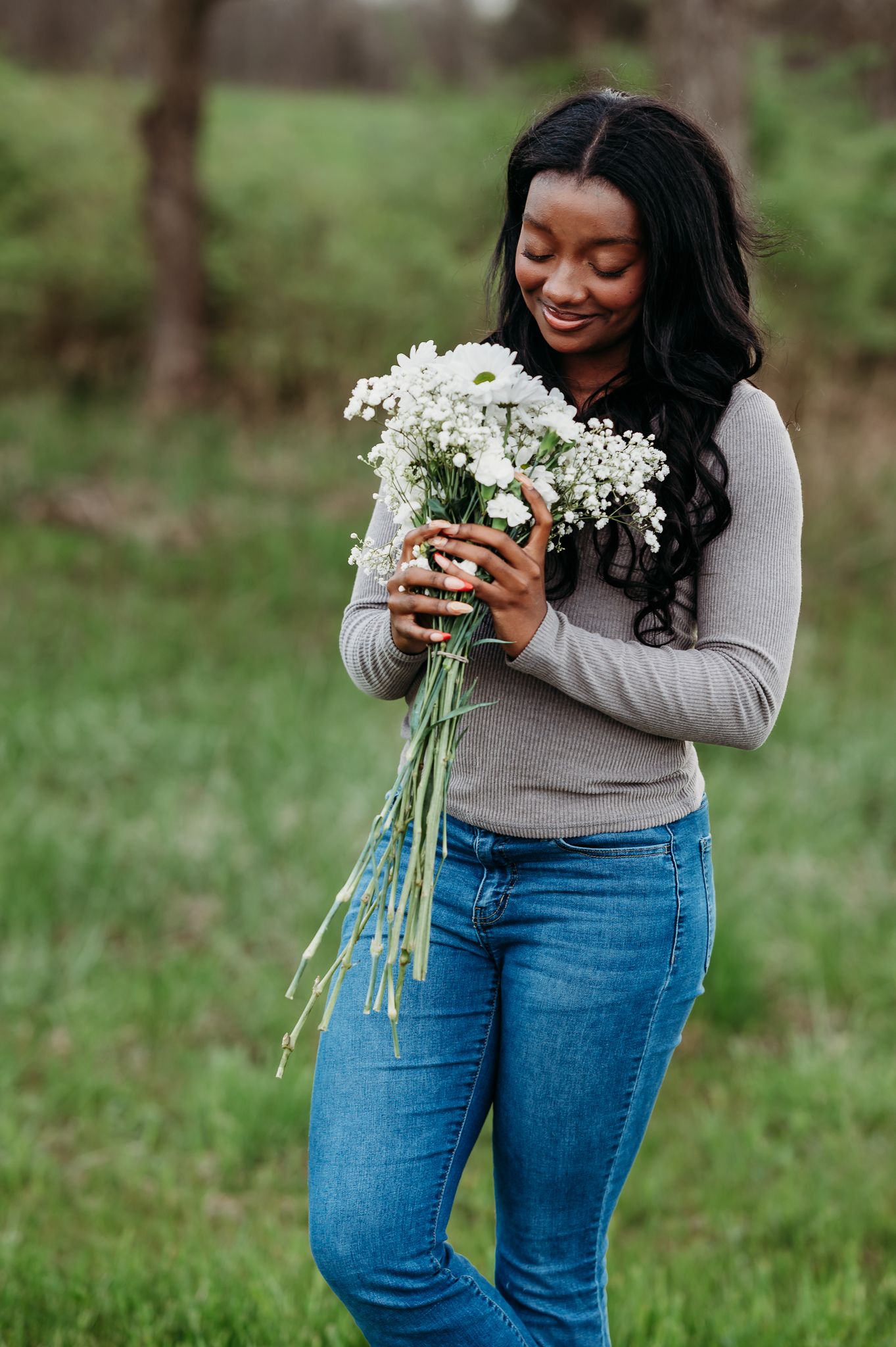 Person in a gray sweater holding a beautiful bouquet of fresh white wildflowers while standing in a grassy field.