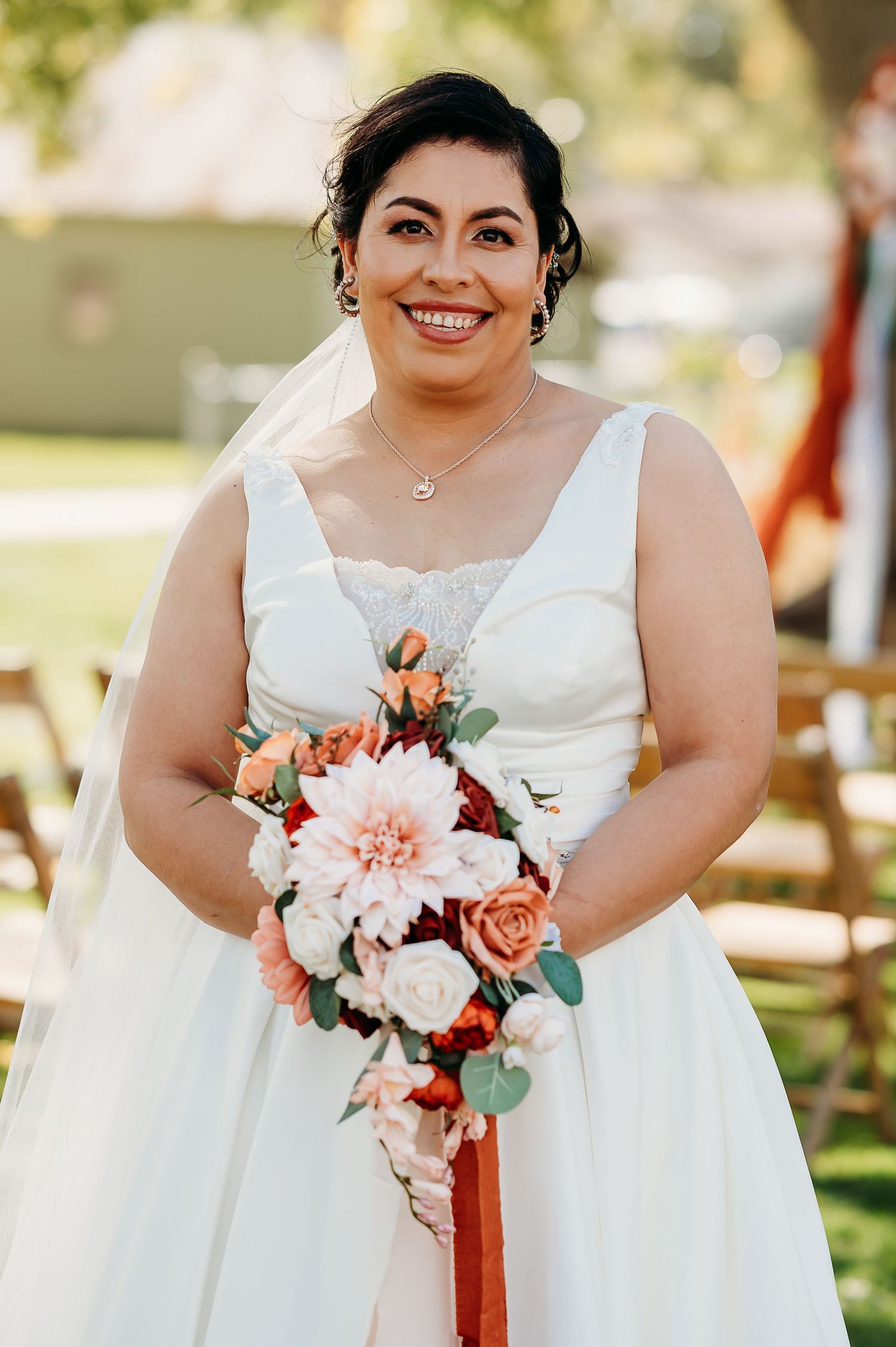 A bride in a white sleeveless wedding gown holds a beautiful bouquet of pink and coral flowers with eucalyptus accents.