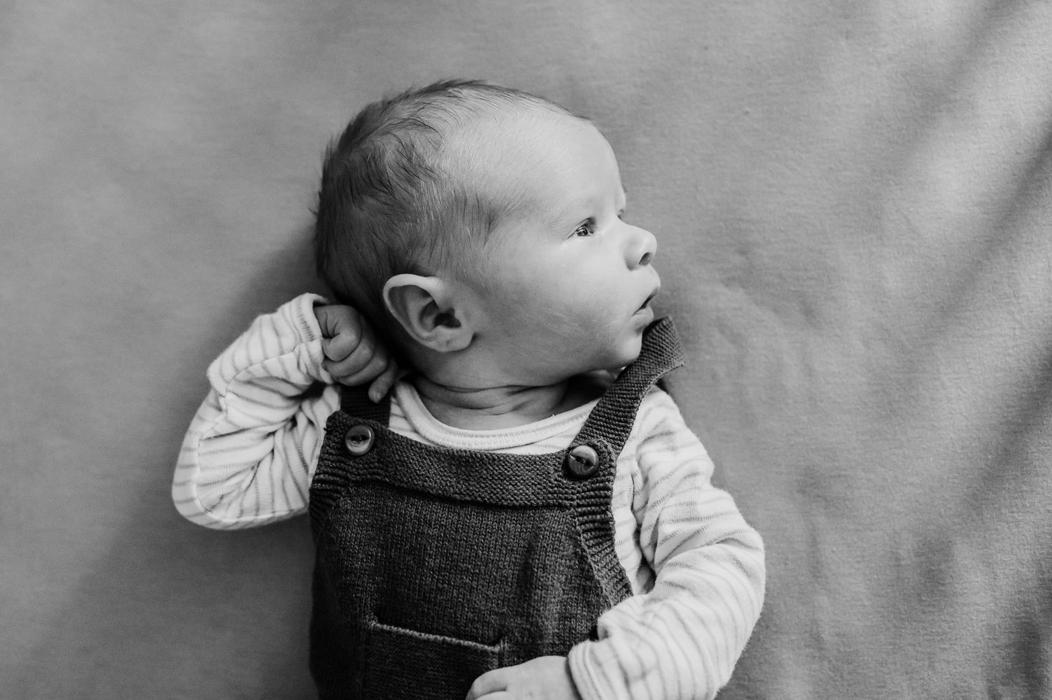 A newborn baby wearing dark jumper lies peacefully in crib during in-home photo session in Indiana with Sara House Photography.