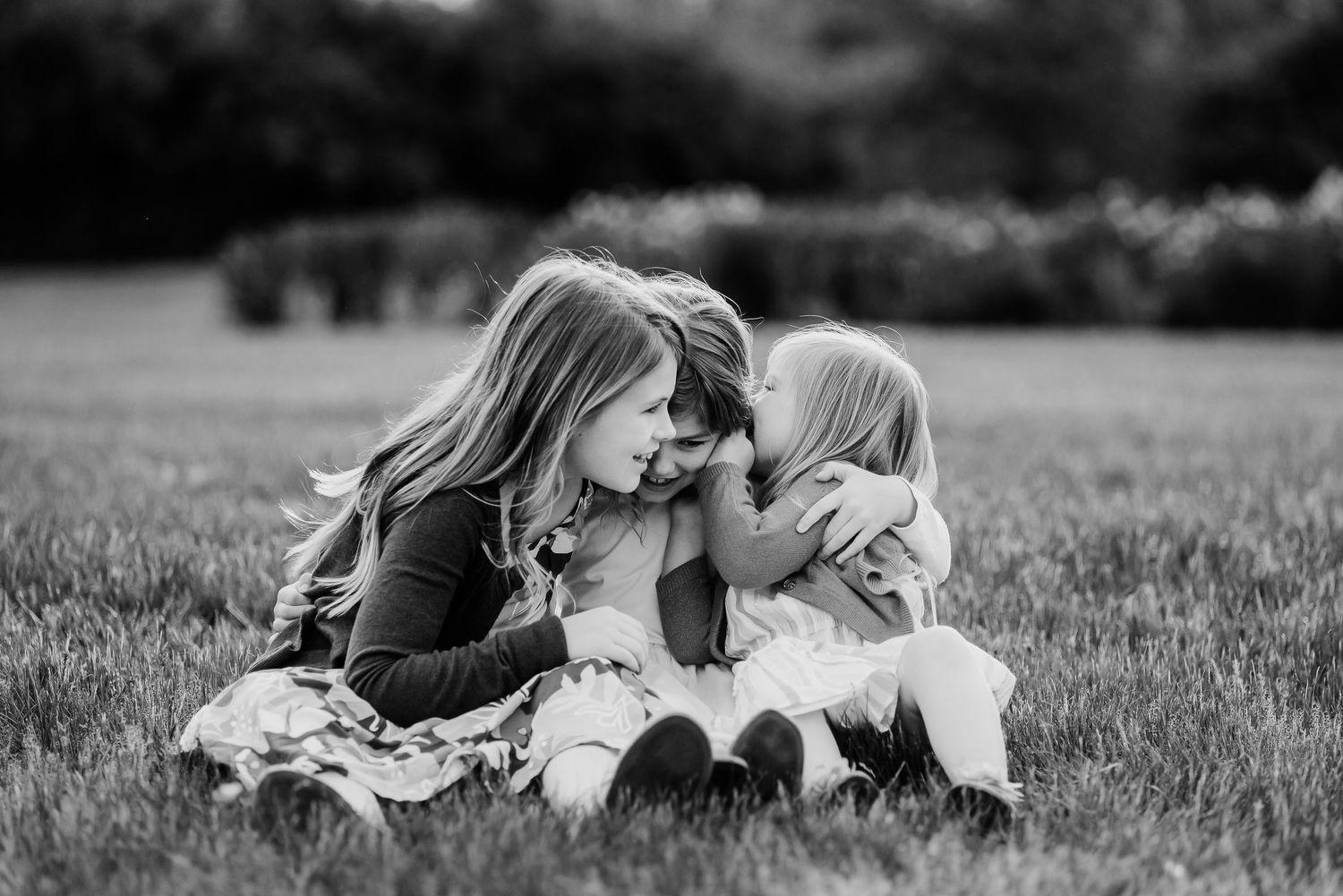 Black and white portrait of three sister sharing a secret during golden hour spring family photo session in Plainfield, Indiana.