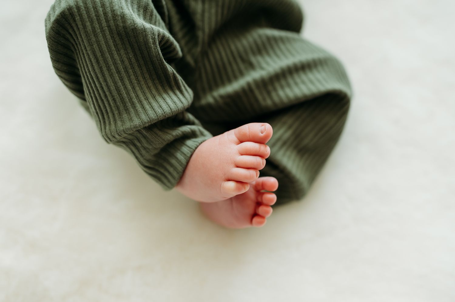 A tiny baby foot with red painted toenails peeks out from green ribbed fabric against a white background.