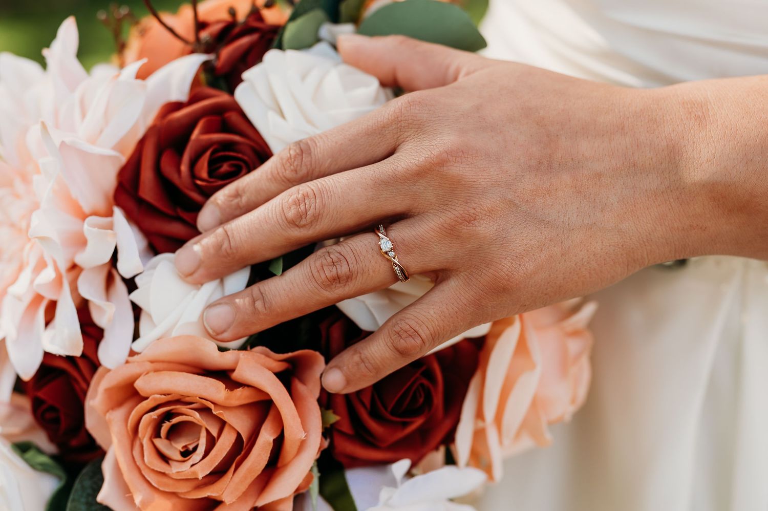 Close-up view of hands exchanging wedding rings with pink and red roses in the background.
