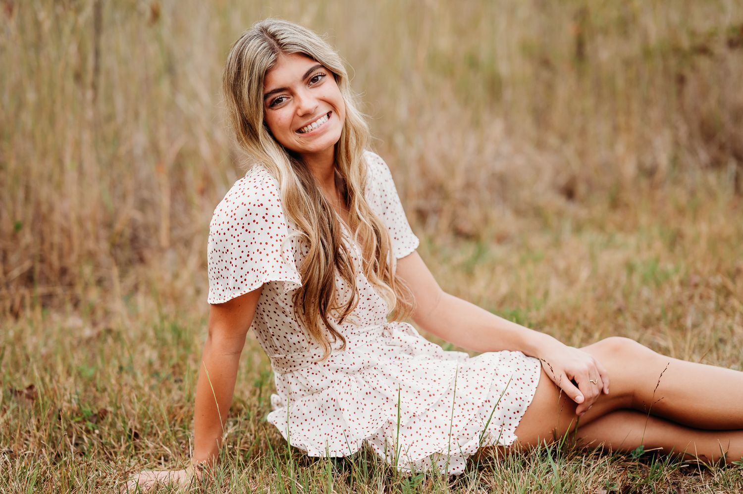 A person in a white lace dress sits in a grassy meadow during golden hour.