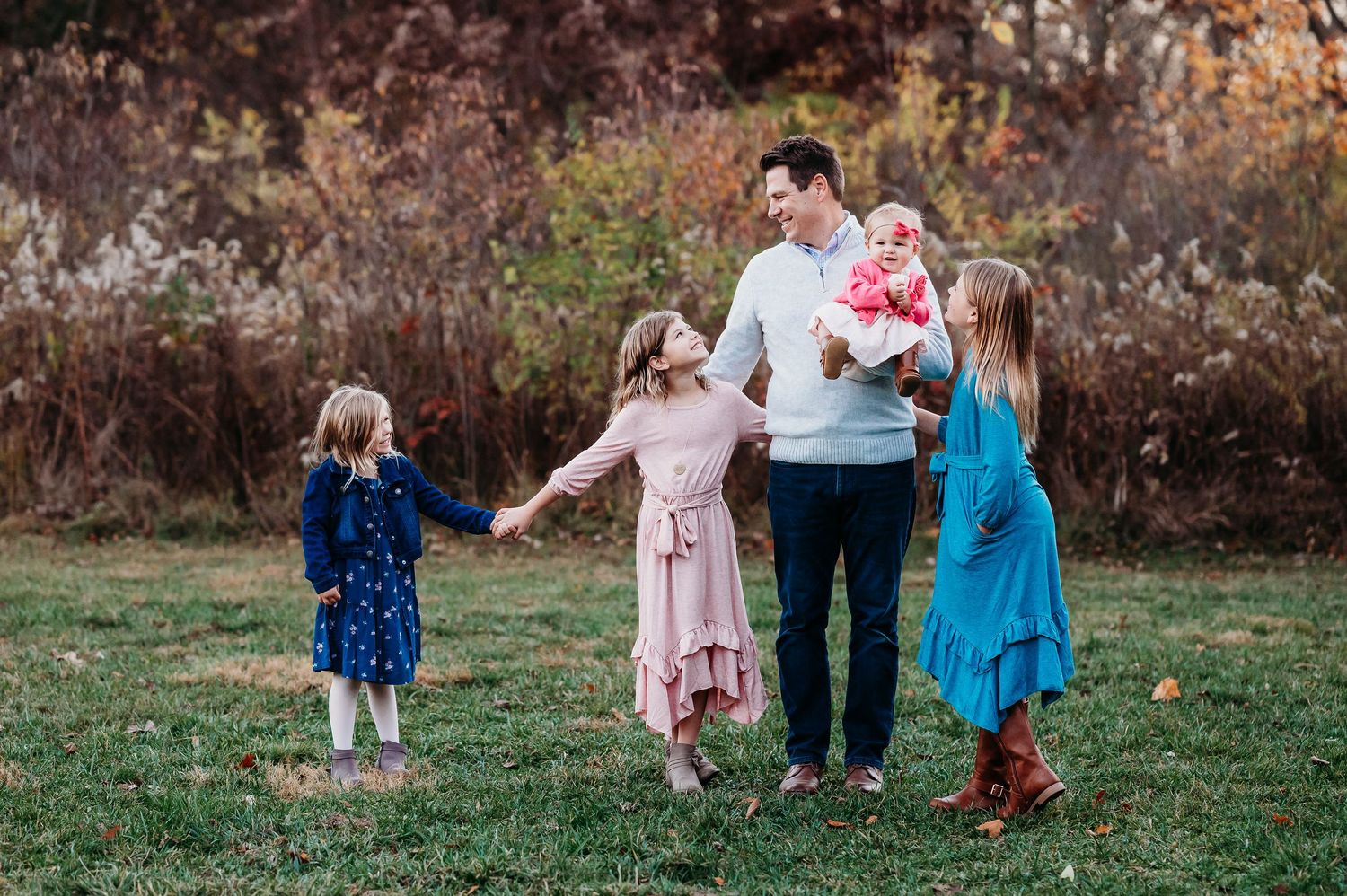 Children playing together with dad in grassy field during autumn photos at Ritchey Woods Nature Preserve in Fishers, Indiana.