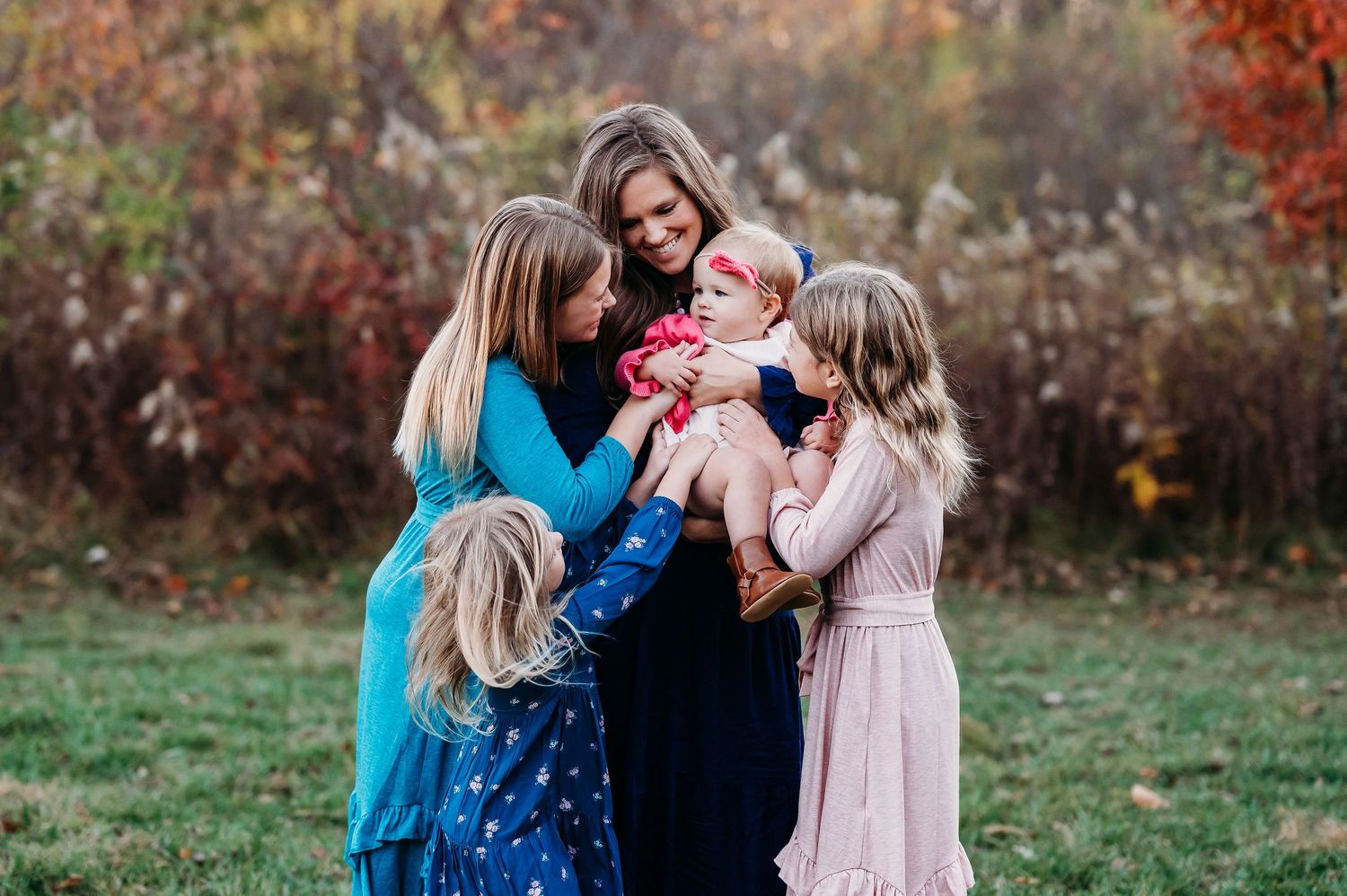 A family wearing coordinated blue and pink outfits poses together during an autumn outdoor photo session at Ritchey Woods Nature Preserve.