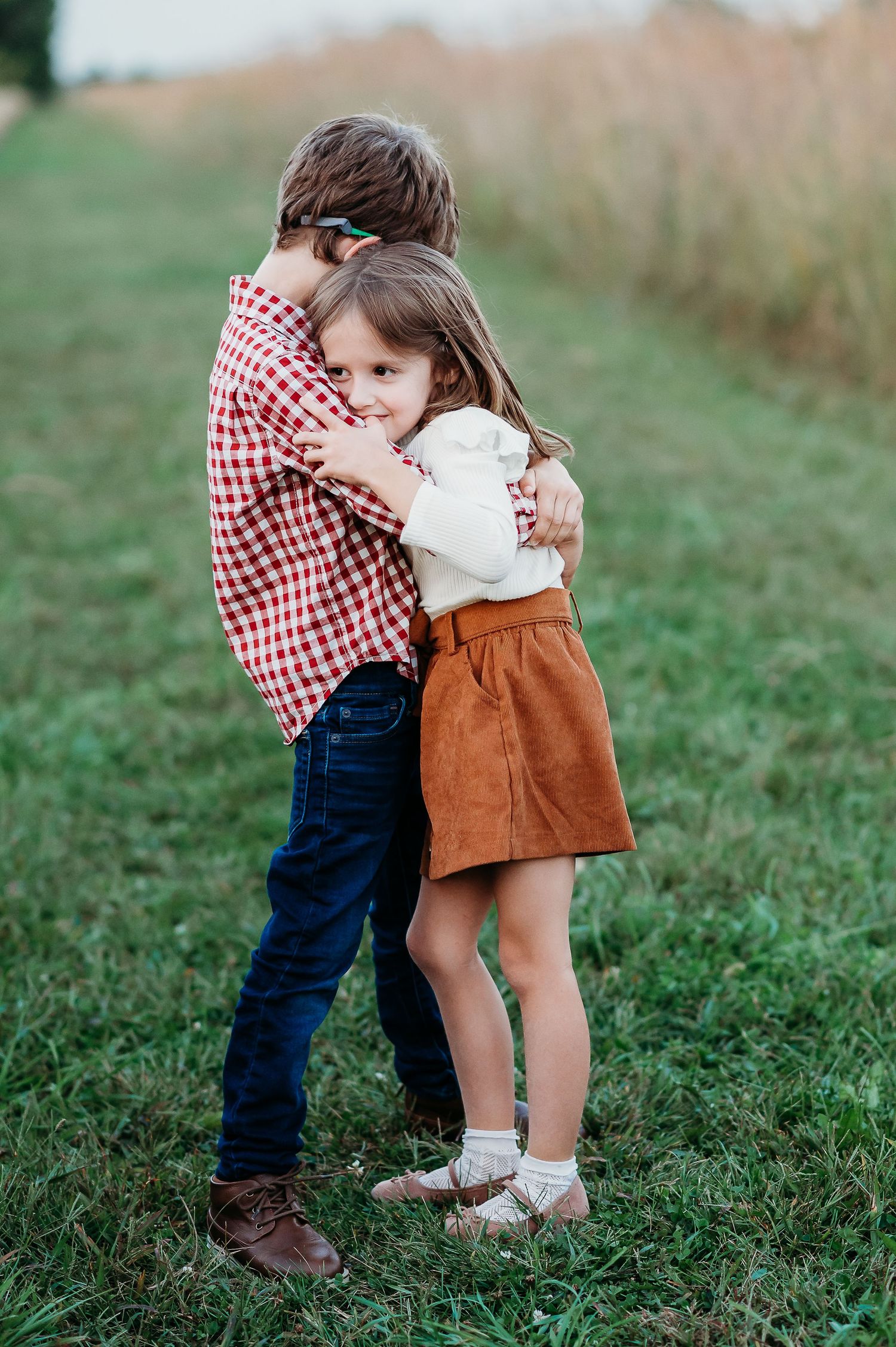 Two young children share a sweet hug outdoors in a grassy field at Prophetstown State Park in West Lafayette, Indiana, during golden hour.