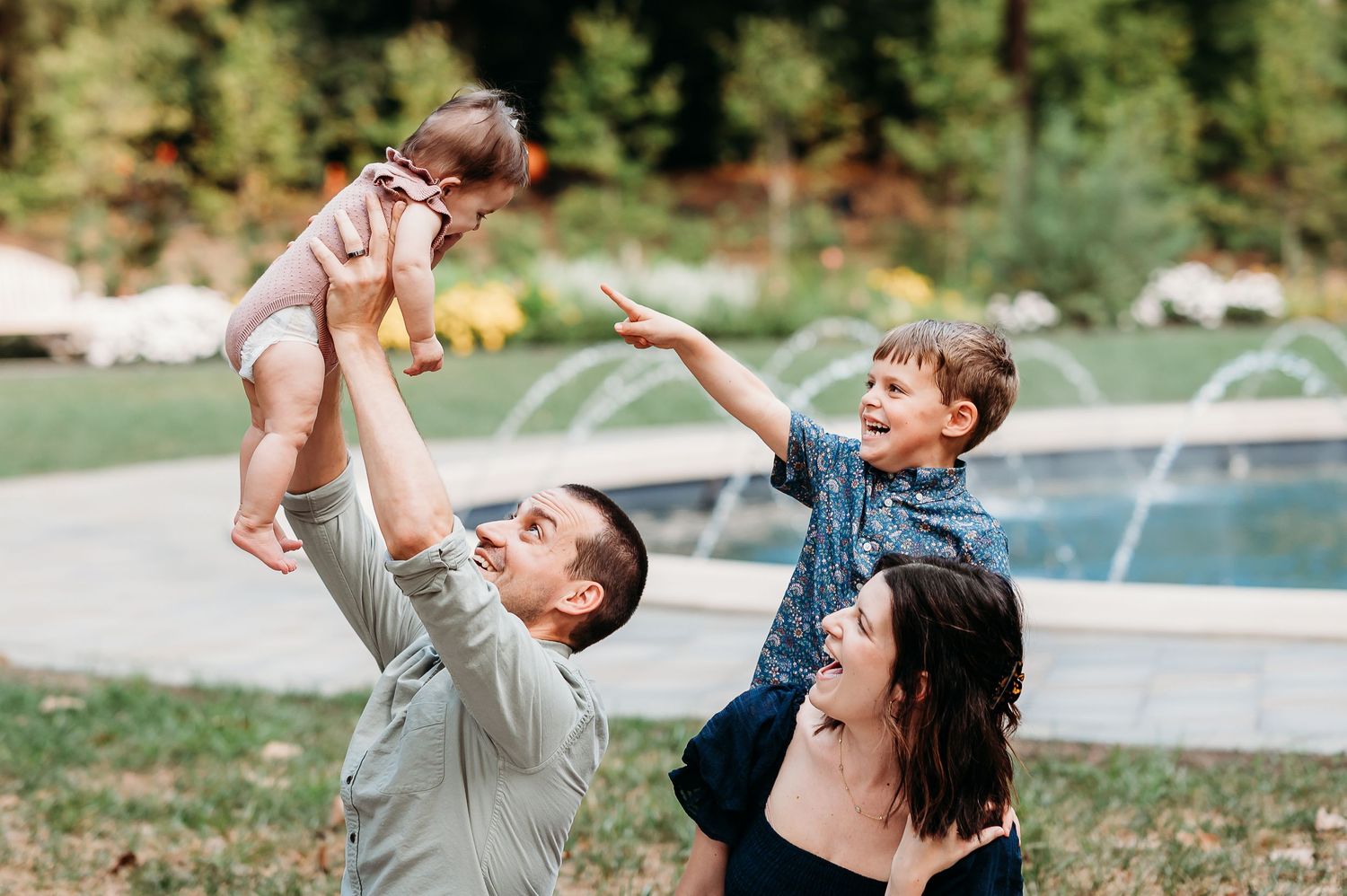 Family laughing together outdoors by fountain during family photo session at Newfields in Indianapolis.