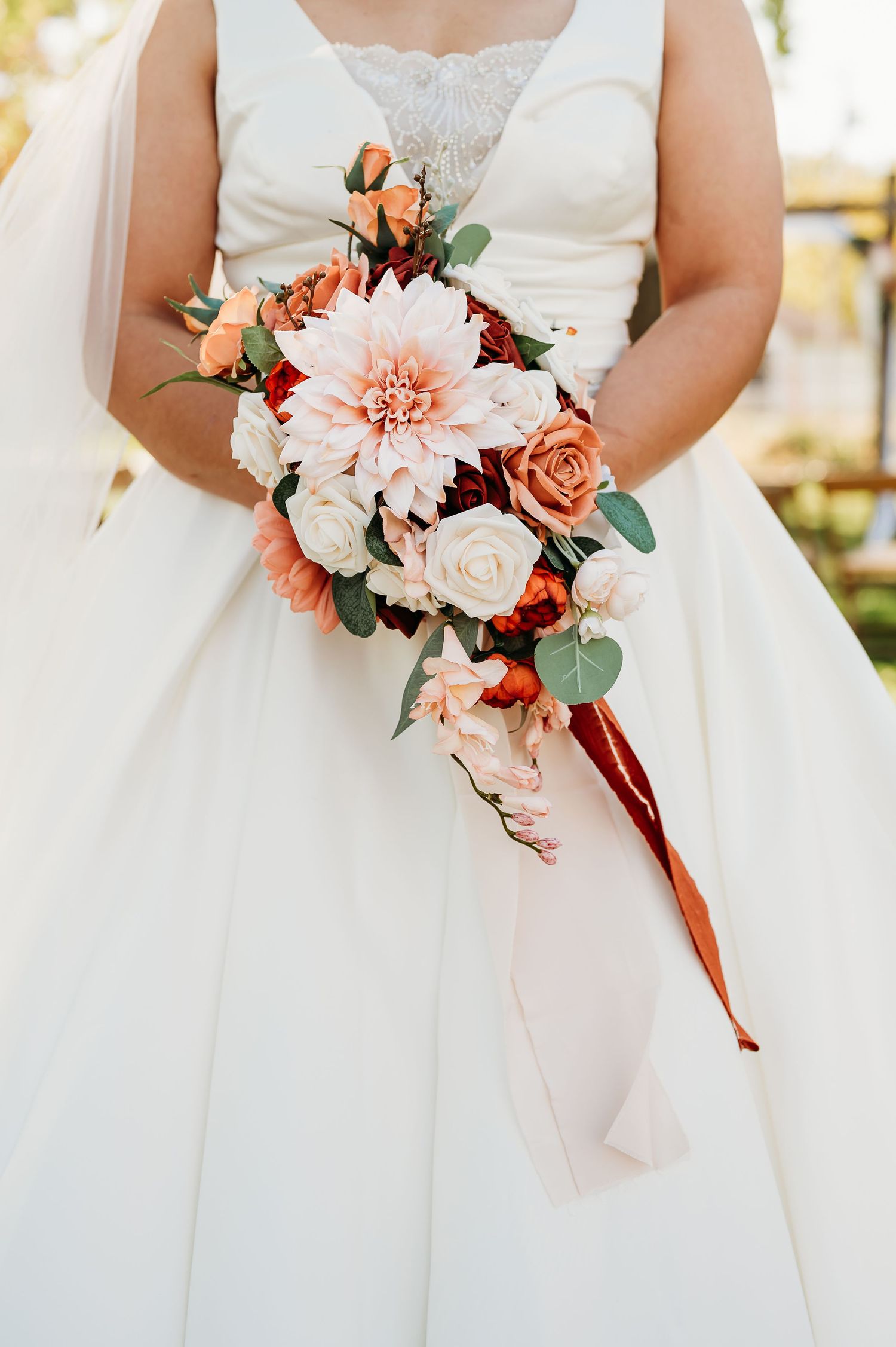 Row of bridesmaids holding coral and white floral bouquets with eucalyptus accents against white dresses.