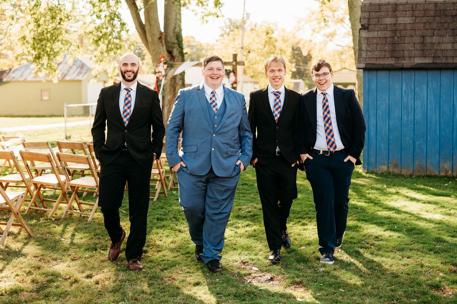 A group in formal attire walks through a sunlit outdoor setting during a wedding celebration.