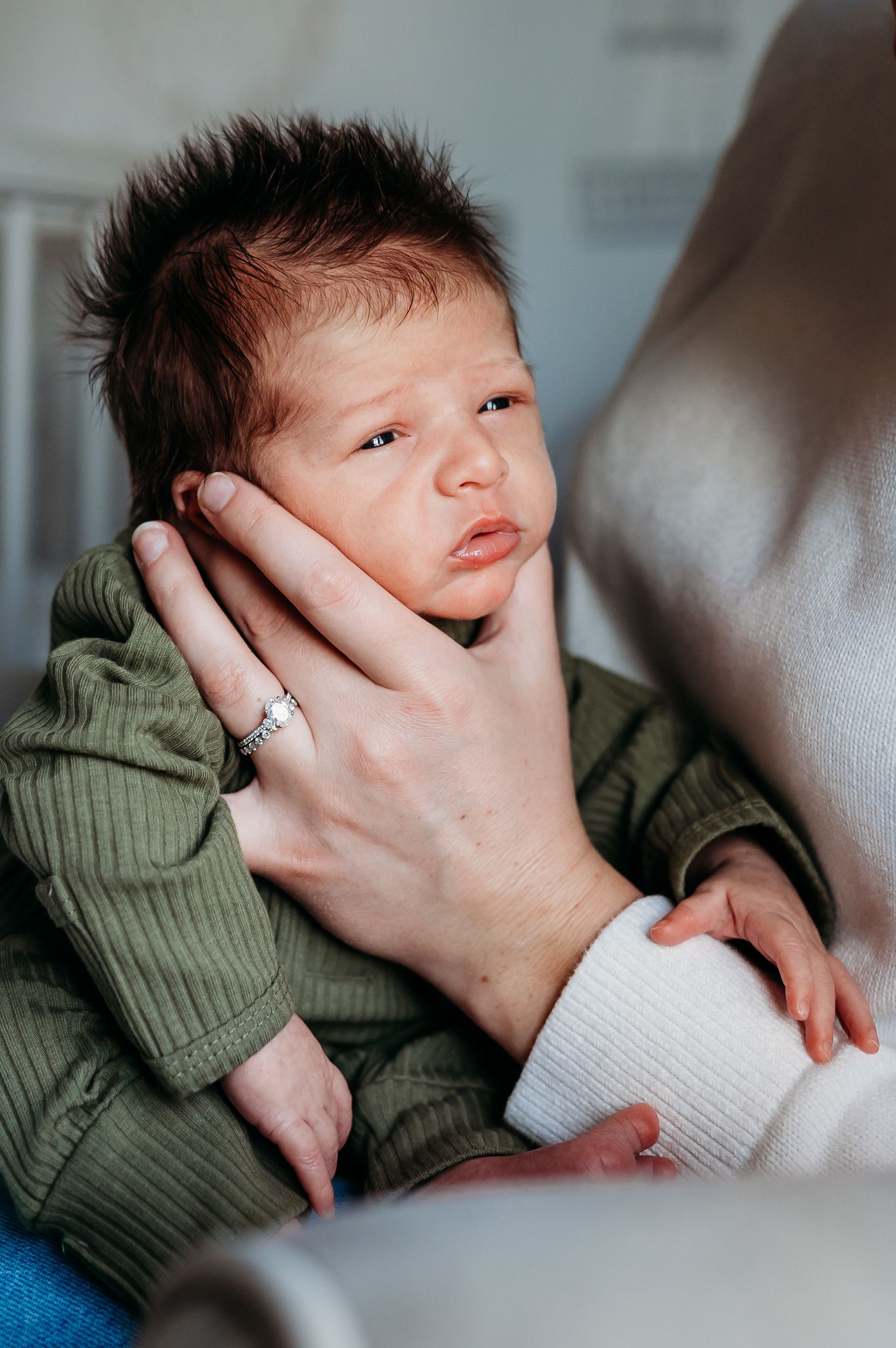 A newborn baby in a green knit sweater is cradled gently in someone's hands during an in-home photo session in Noblesville, Indiana.