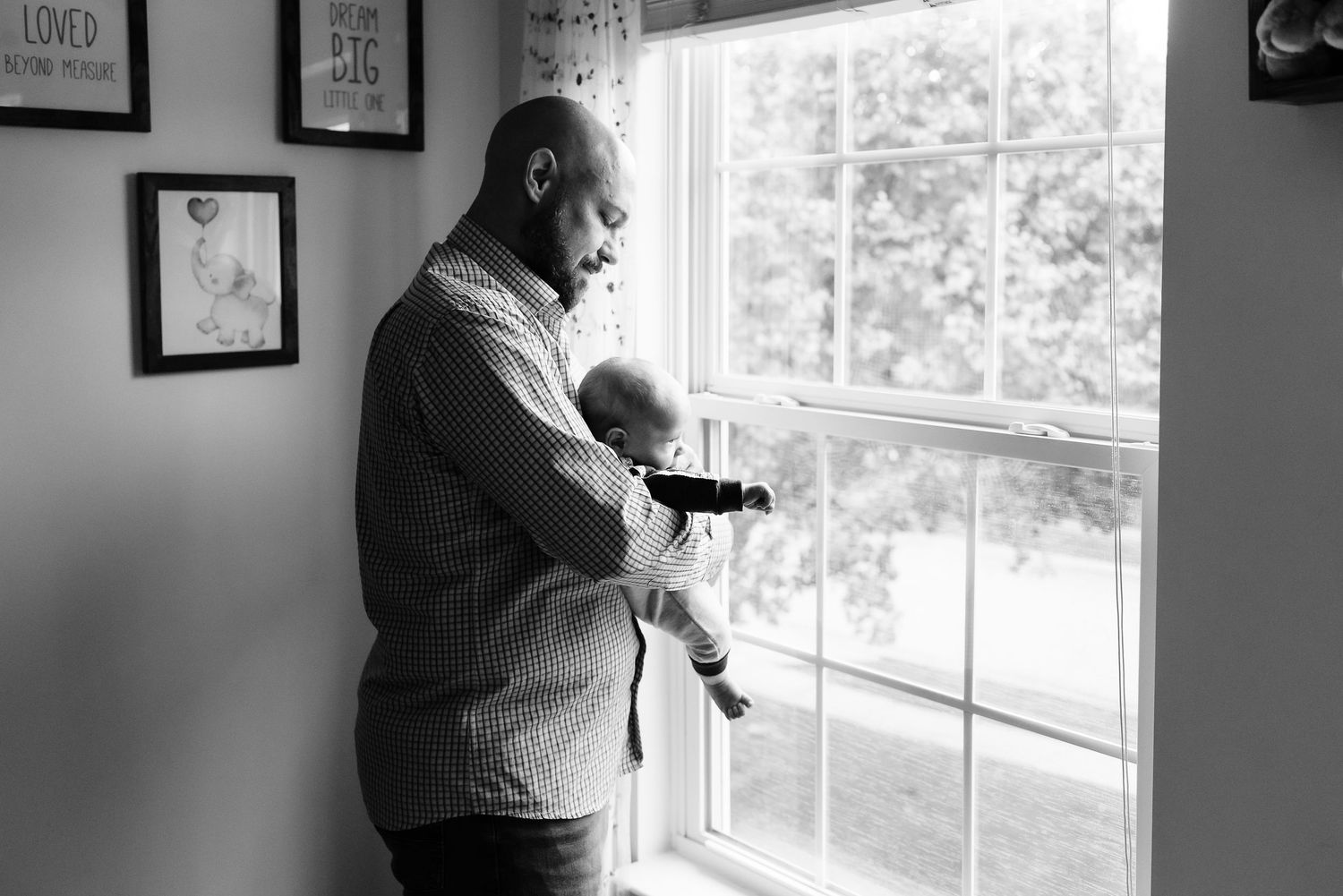 A tender black and white moment by a window as a parent holds their baby in natural light.