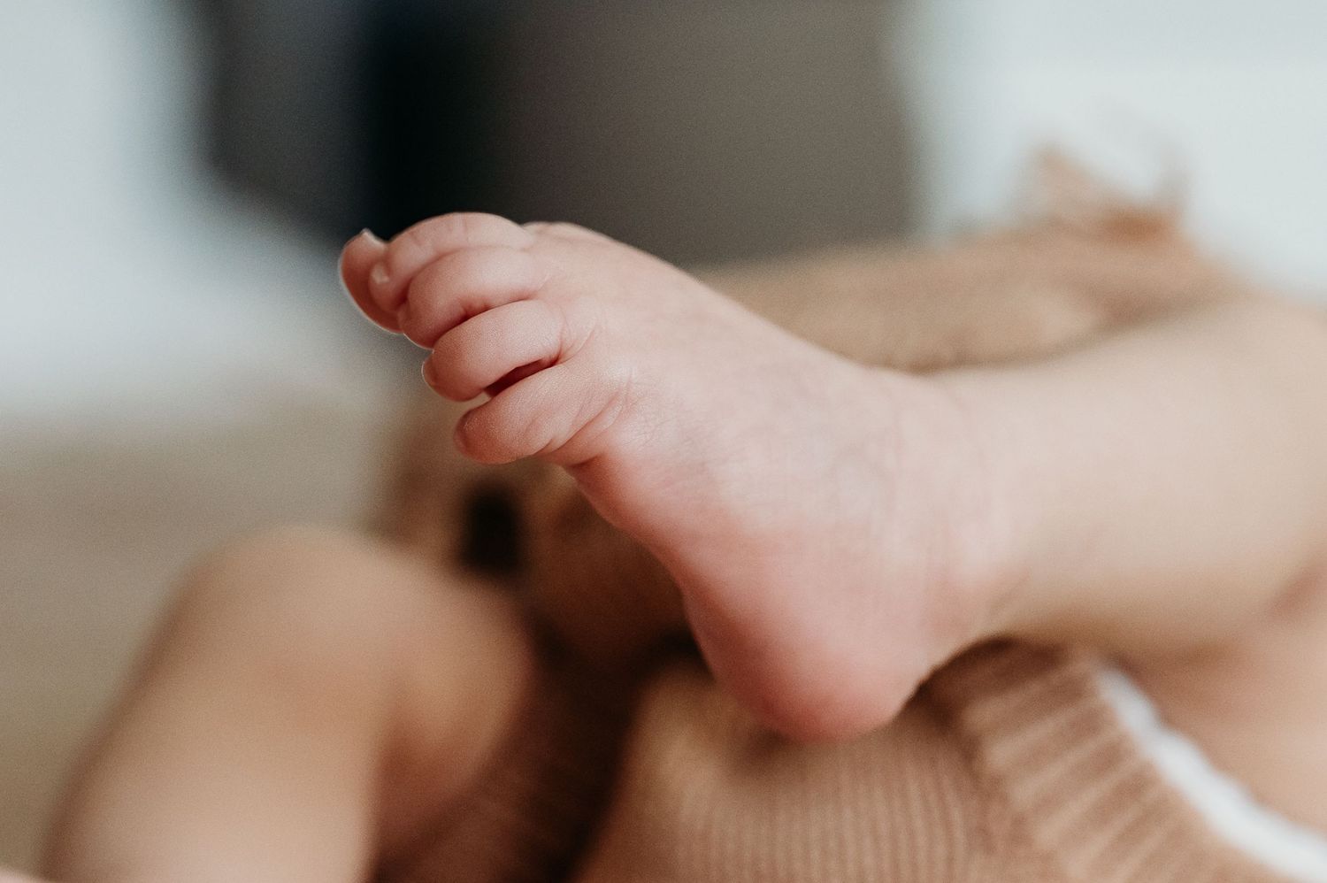 Close-up of a newborn baby's tiny foot and toes resting on a soft beige knit blanket.