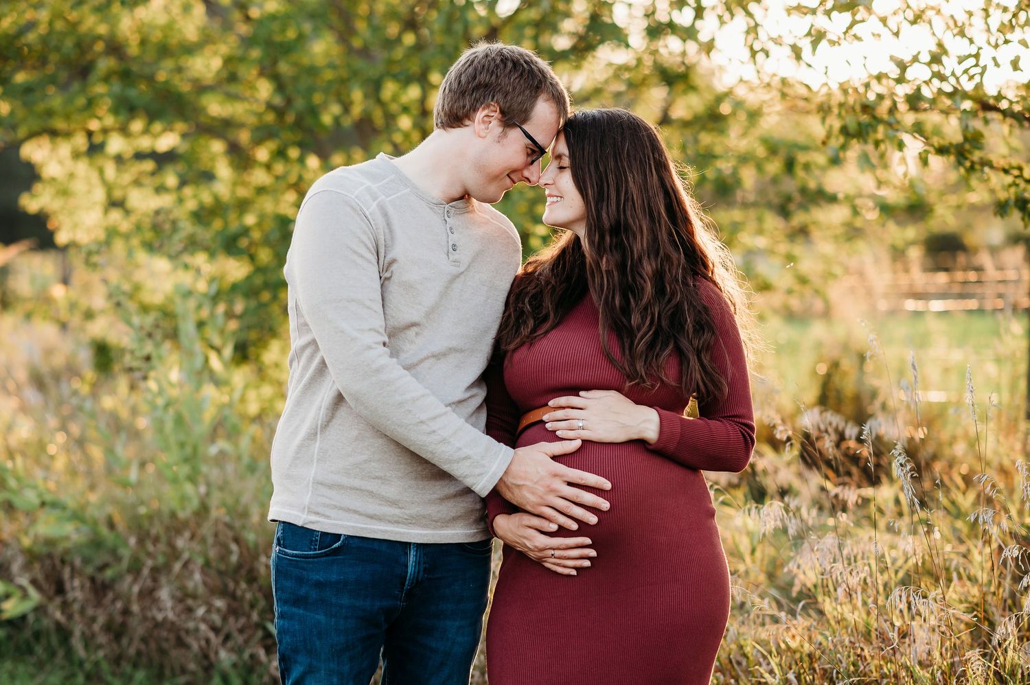 An expecting couple embraces at Prophetstown State Park in West Lafayette, Indiana during sunset while wearing burgundy and beige clothing.