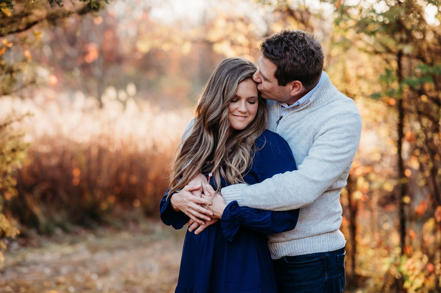 Romantic couple shares intimate moment outdoors during golden hour with warm autumn colors in background in Fishers, Indiana.