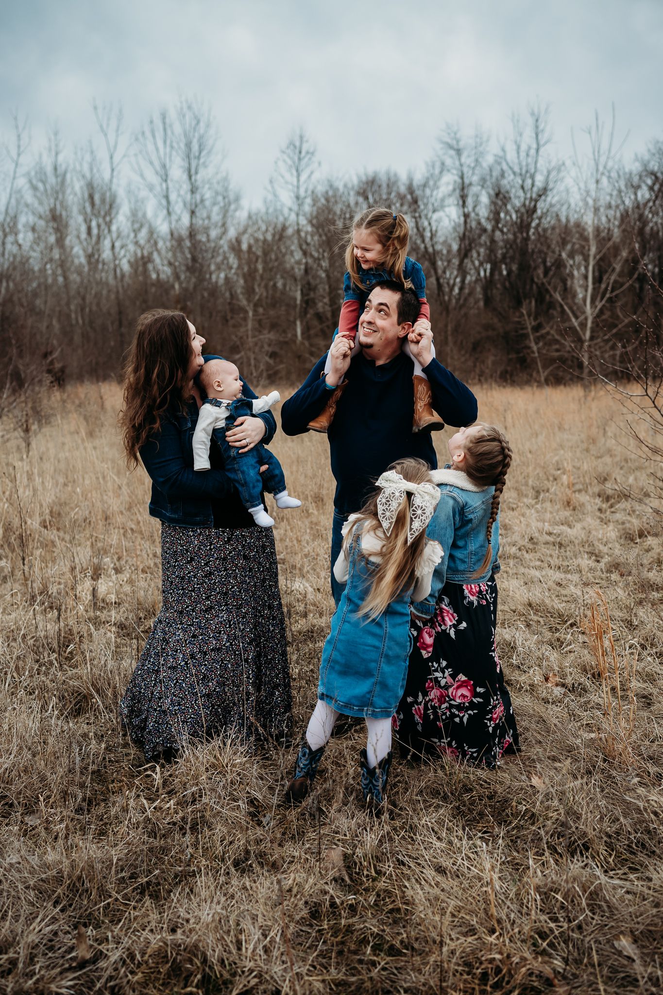 A family of six plays and dances together in a field of tall brown grass during Avon, Indiana, family photo session.