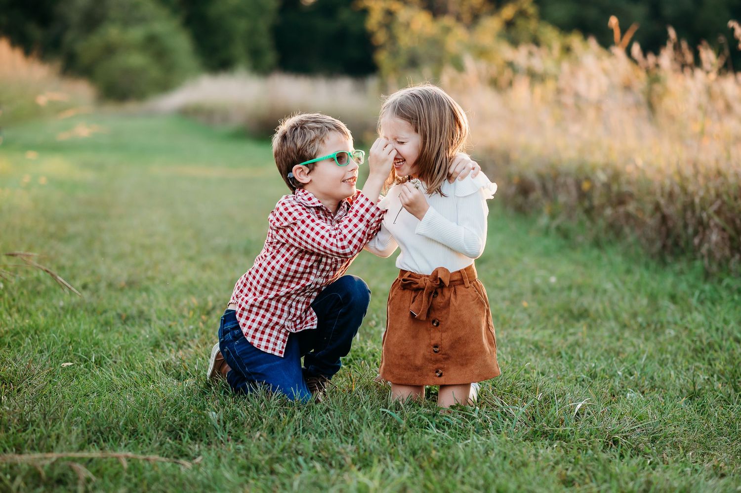 Two young children in autumn clothing sit together in grassy during golden hour sunset at Prophetstown State Park in West Lafayette, Indiana