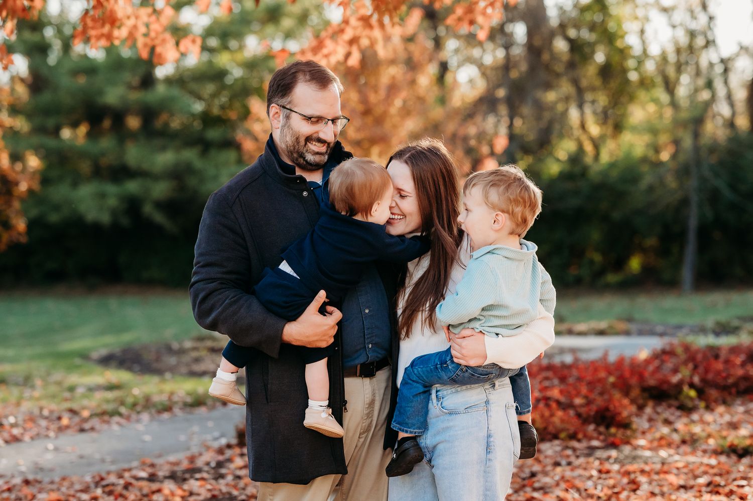 Family enjoying a playful autumn photoshoot outdoors with colorful fall foliage in the background  at Friendship Gardens in Plainfield.