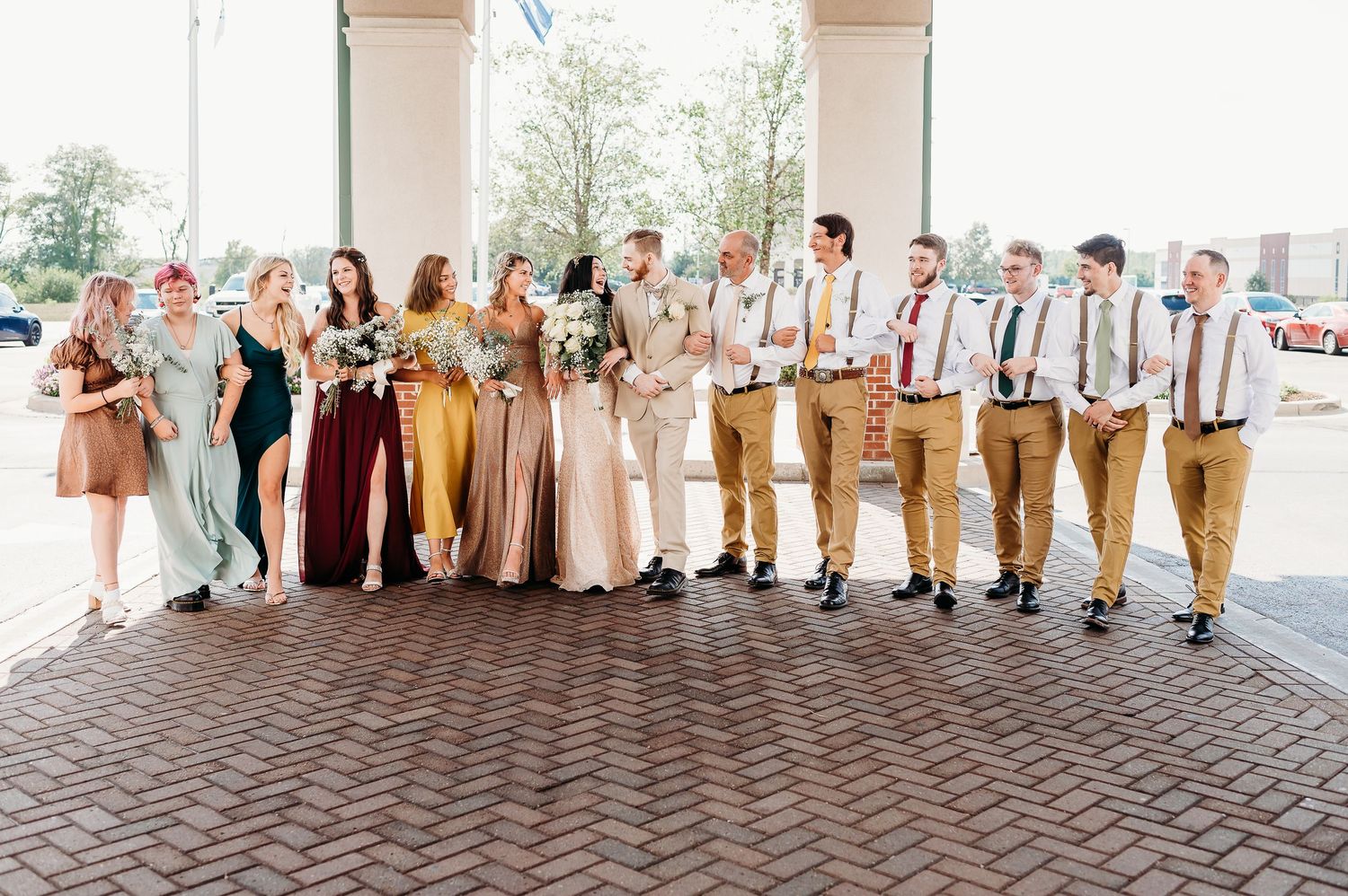 Wedding party members in coordinated earth tone and neutral colored attire pose together in an outdoor setting.