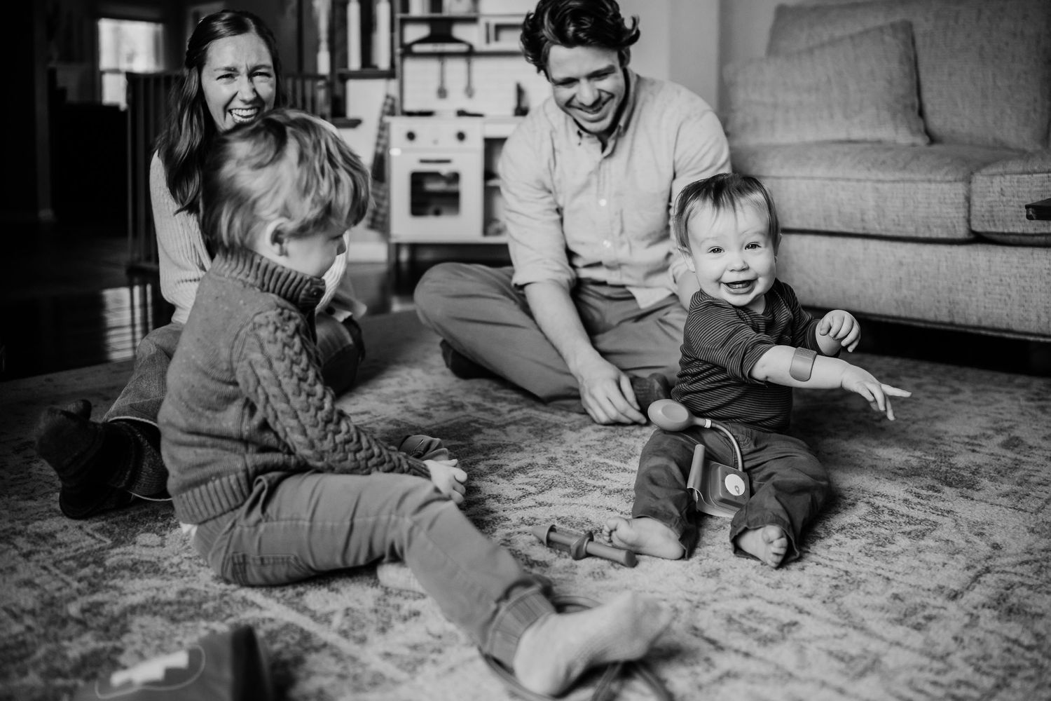 Black and white photo of a happy family with two young children playing together on a living room floor.