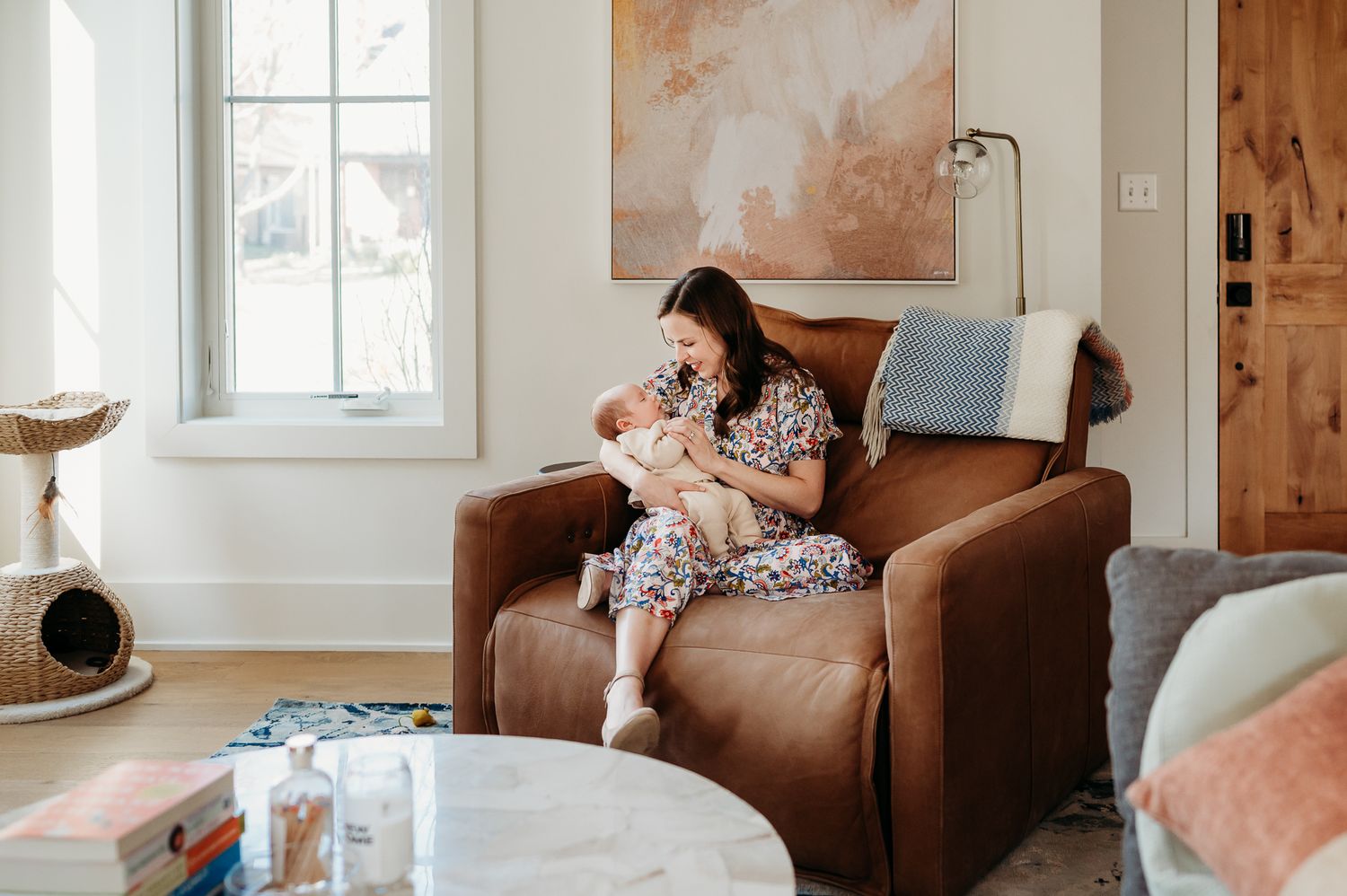 Mother sits in a brown leather armchair cuddling a baby in a cozy living room with natural lighting in Westfield home.