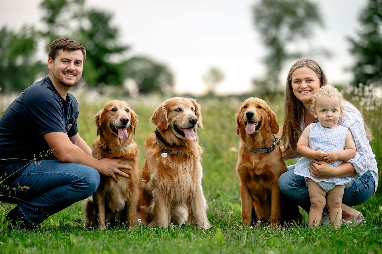Smiling family with baby and three golden retrievers pose on green grass during session with Hendricks County Pet Photographer Sara House.
