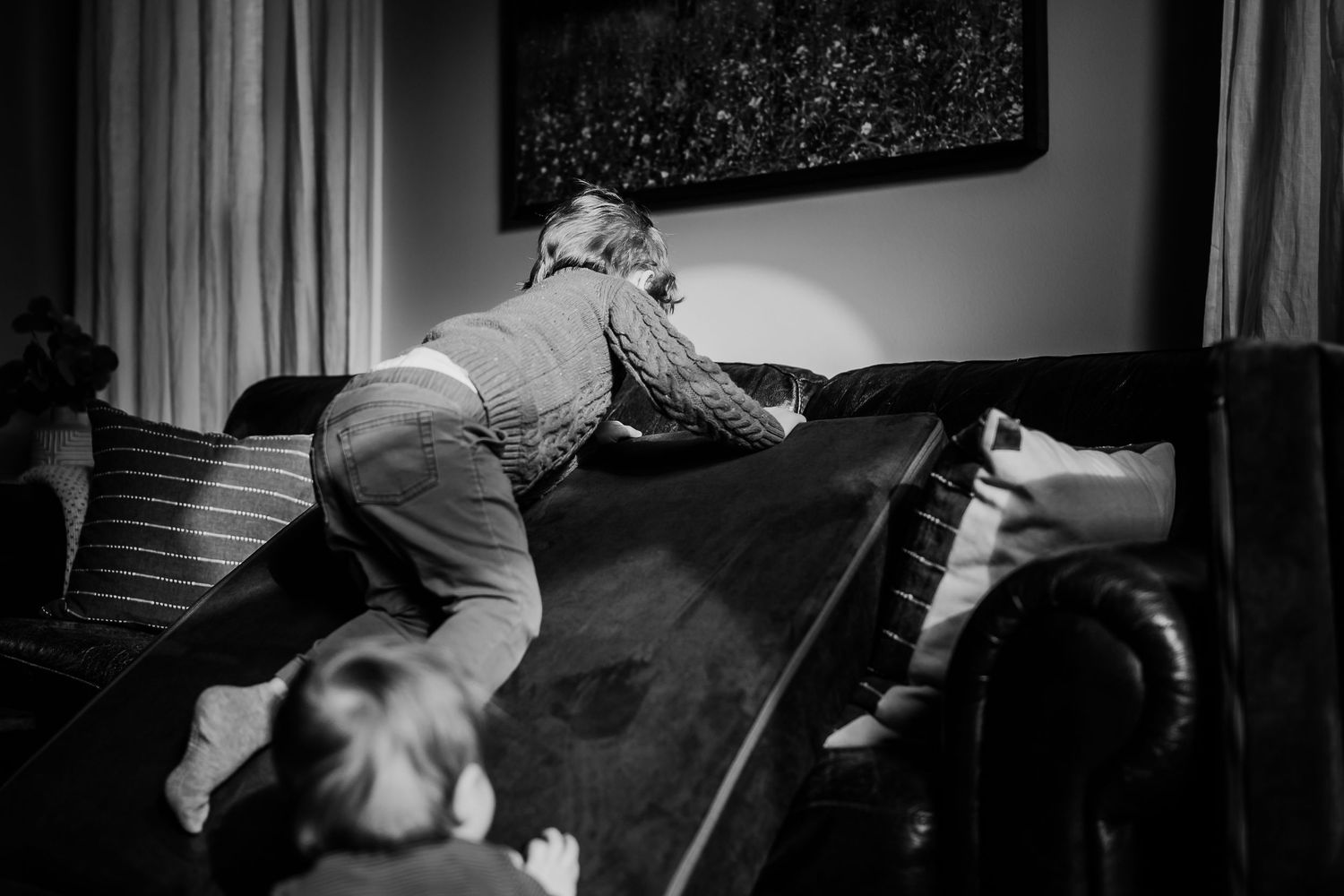 Black and white photo of a boy climbing over slide cushions while a child watches in a cozy Indianapolis living room.