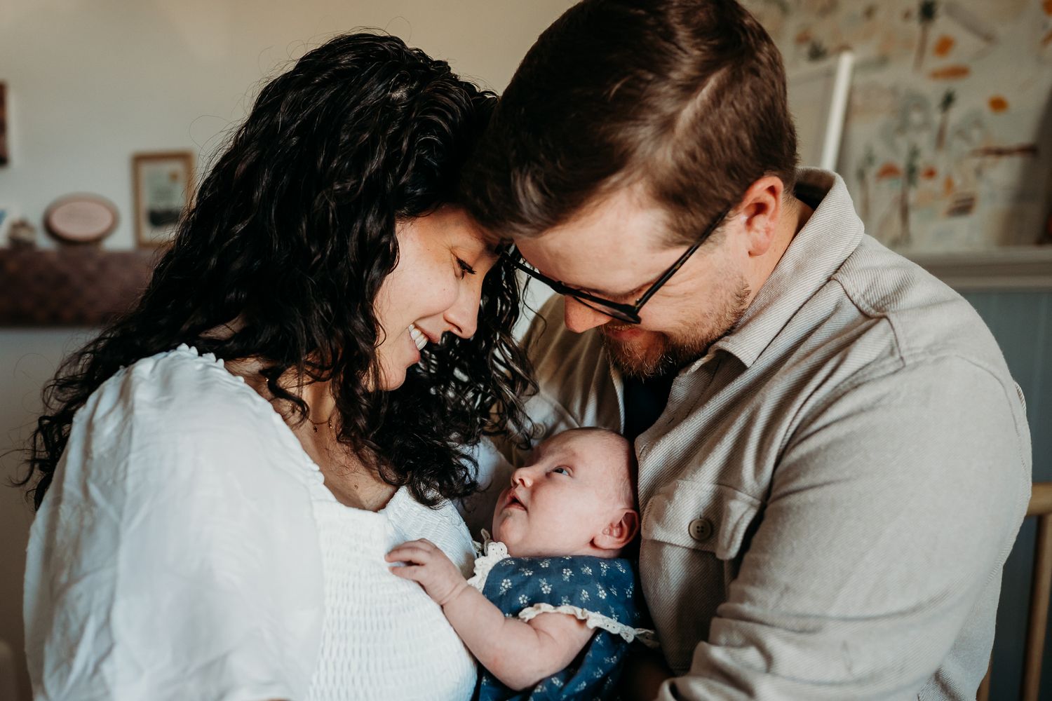An emotional lifestyle photograph showing a family embracing baby girl in soft natural light in their Westfield, Indiana, home nursery.