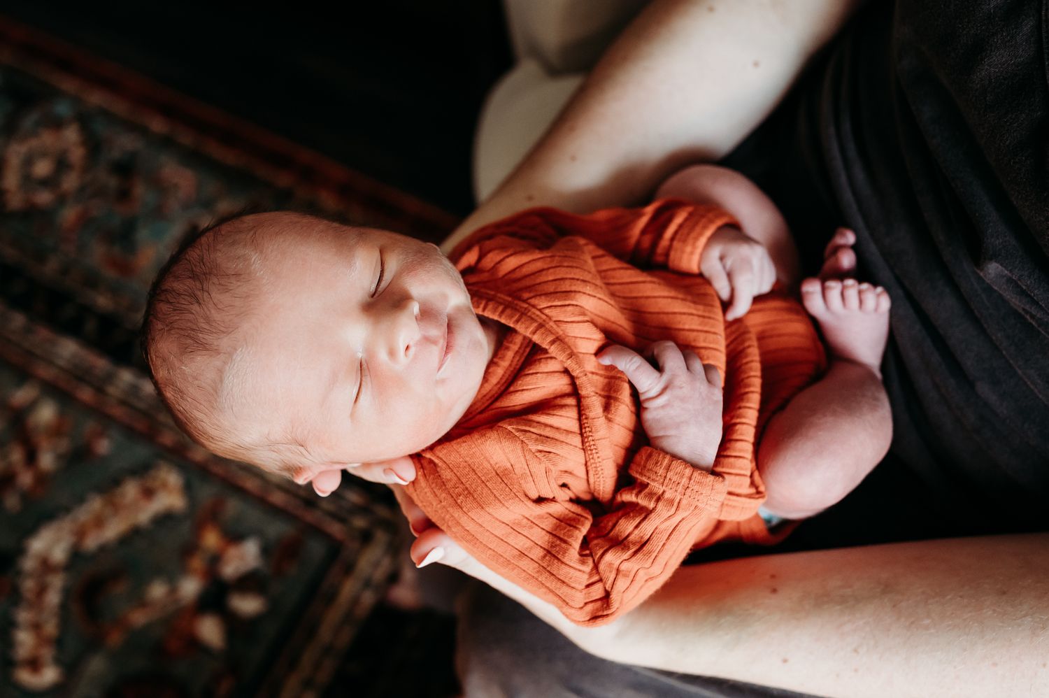 A sleeping infant wearing a soft orange outfit rests in mom's arms during Indiana in-home newborn photo session with Sara House Photography.