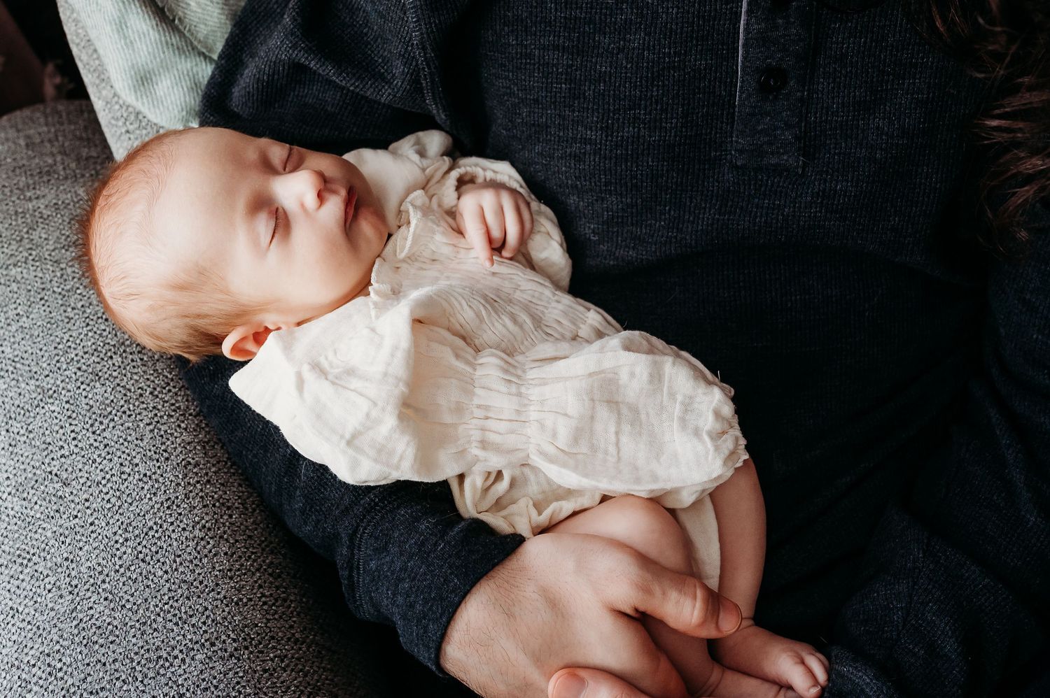A sleeping baby girl wearing a cream outfit rests peacefully in father's arms in Noblesville home.