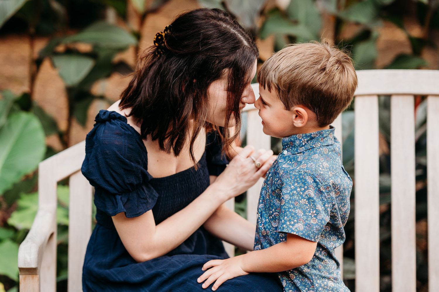 Mom laughs with little boy while sitting on a white wooden bench in a garden setting at Newfields in Indianapolis.