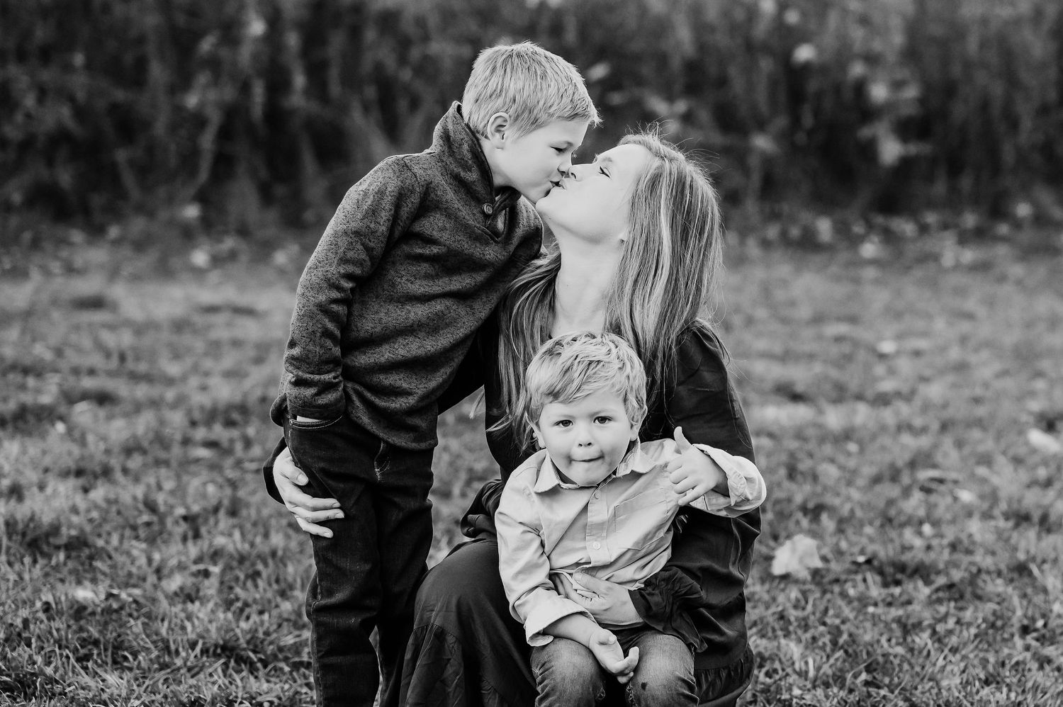 A black and white image of mom and sons outdoors showing affection and connection during Fishers family fall photoshoot.