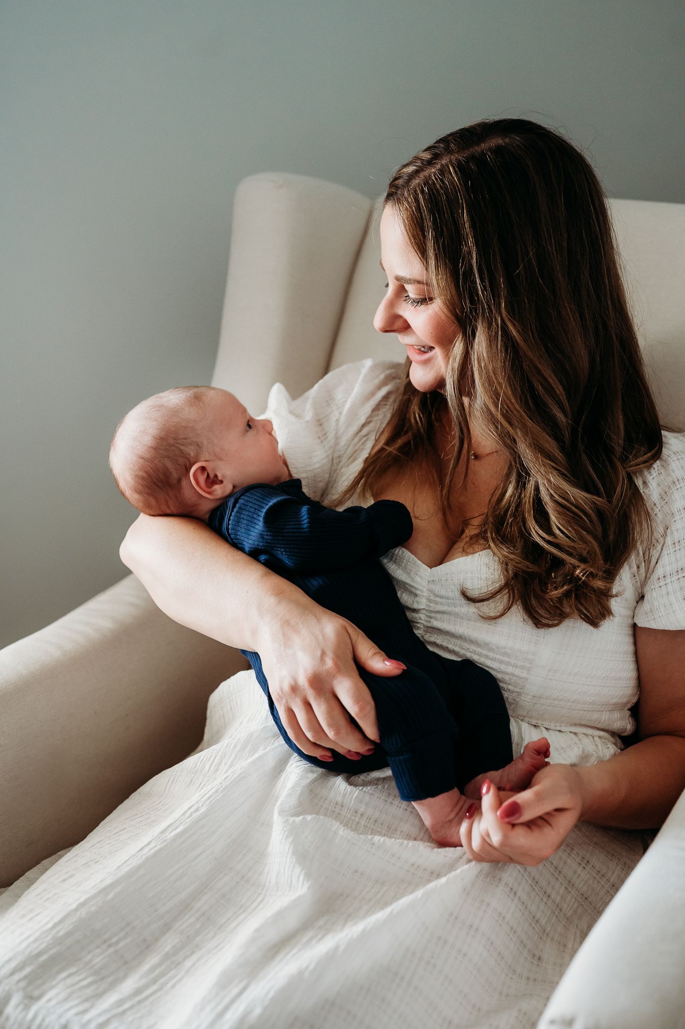 Mother and baby share tender moments together on white rocking chair during Carmel lifestyle newborn photography session.