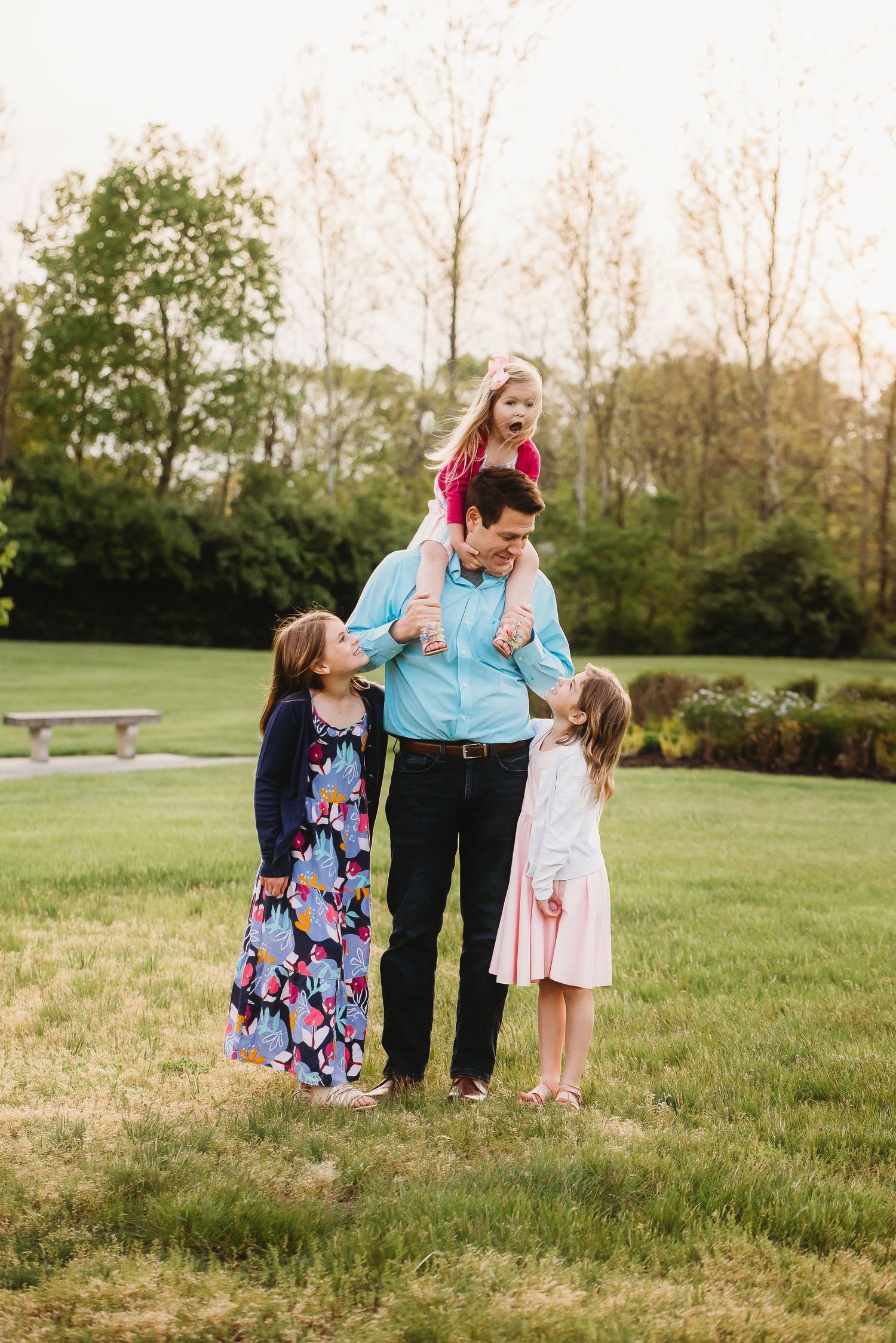 A playful family moment captured outdoors with coordinated outfits in pink, blue and floral patterns.