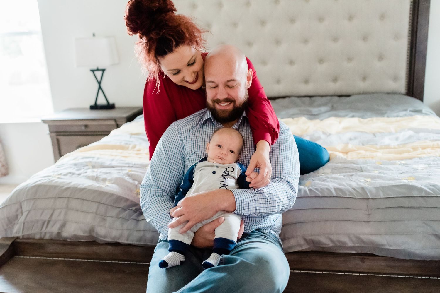 A family shares a joyful moment together with newborn while relaxing on a tufted headboard bed during photoshoot in Avon, Indiana.