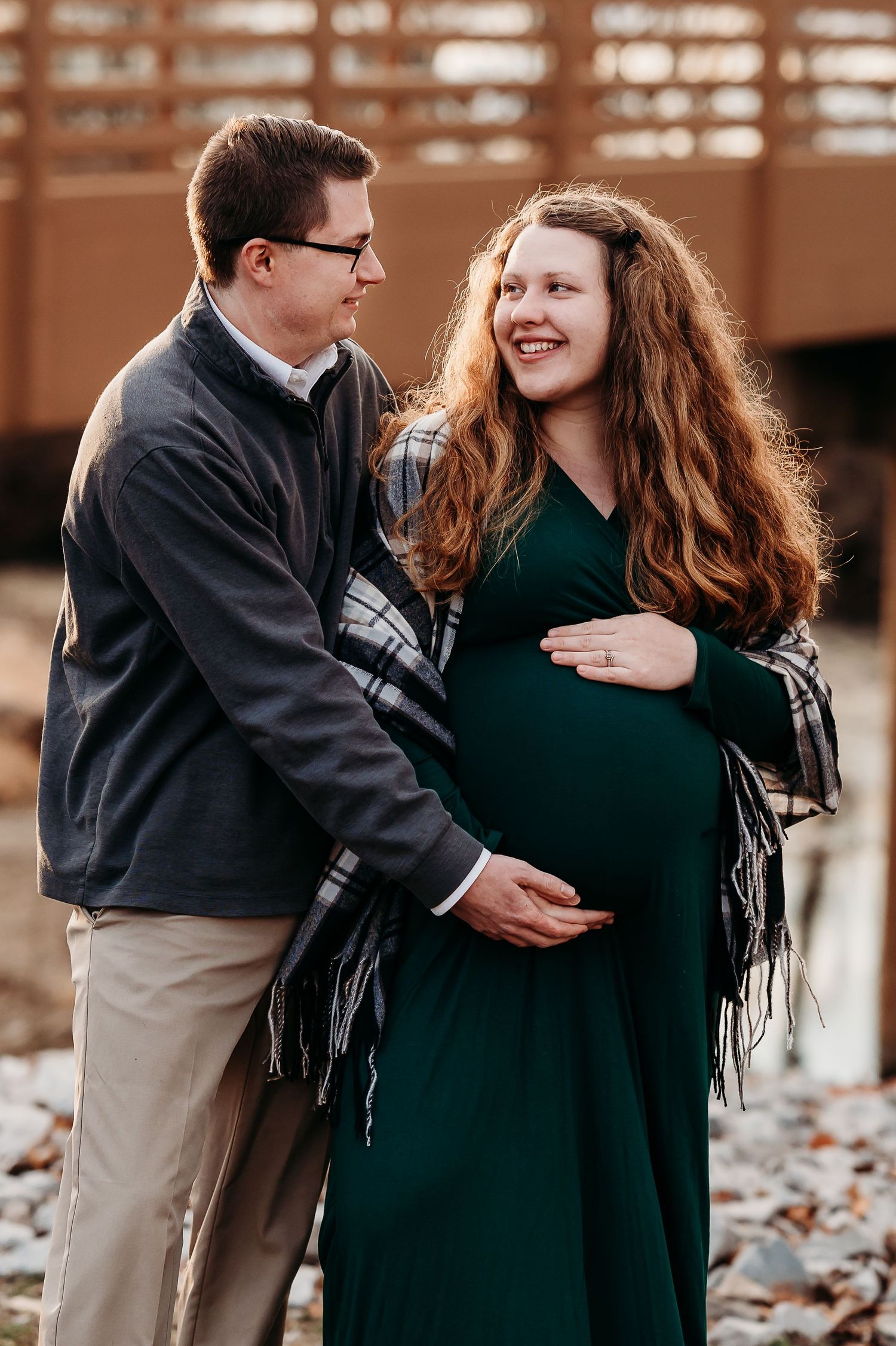 Couple sharing a tender maternity moment outdoors, woman in green dress cradling baby bump, man embracing her warmly.