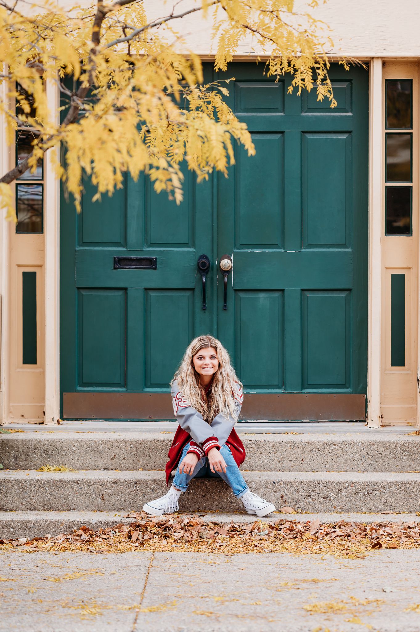 Autumn scene with yellow ginkgo leaves framing a teal colored door entrance as someone sits on stone steps.