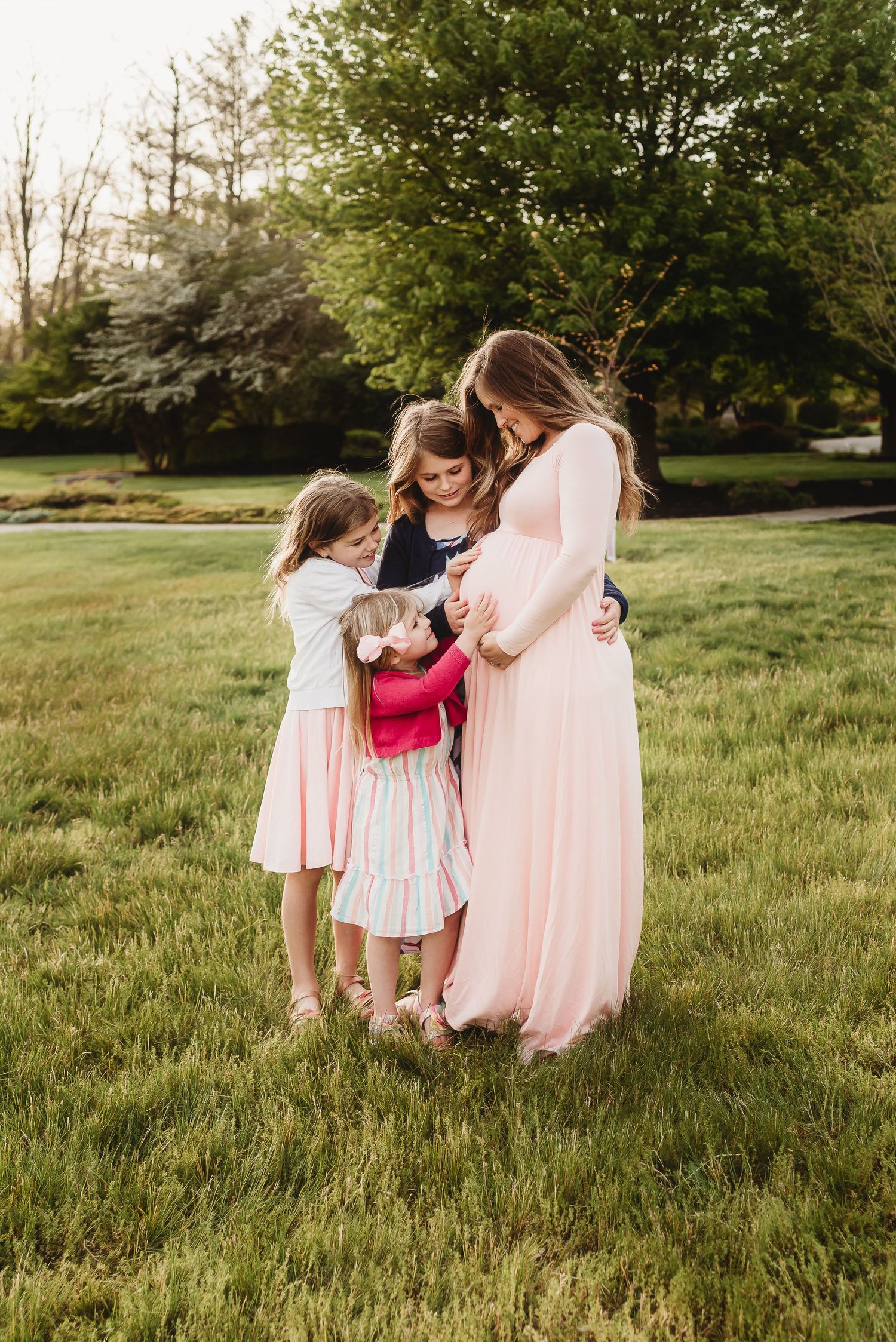 Children in pink and white dresses play together in a sunlit grassy field during springtime.