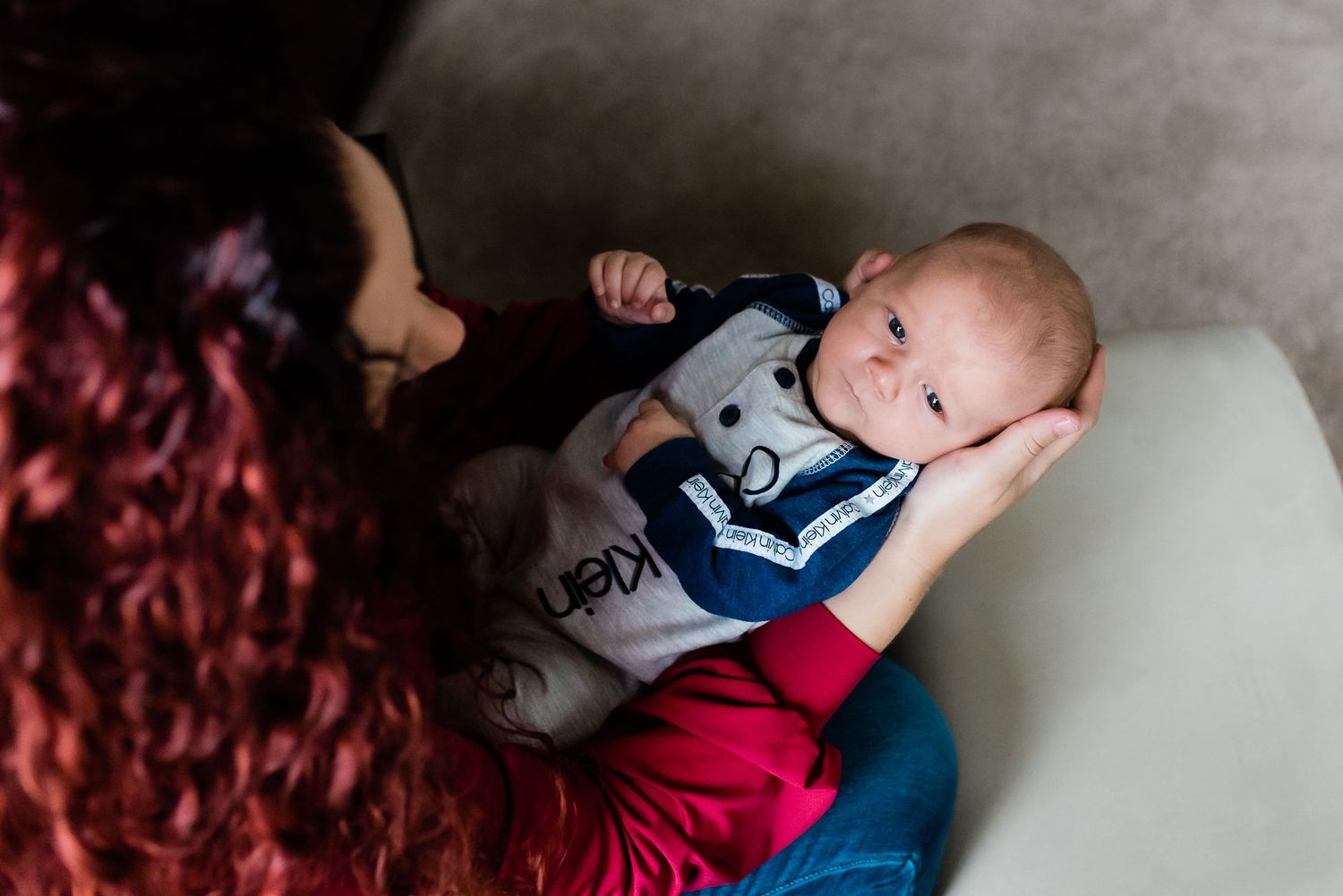 A baby boy lies peacefully in mother's lap while wearing a white and blue striped outfit.