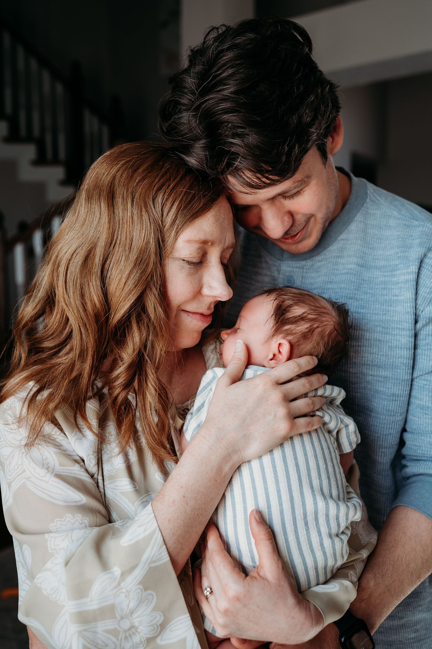 A tender family moment as parents share loving embraces with their newborn baby during in-home photos with Indianapolis newborn photographer