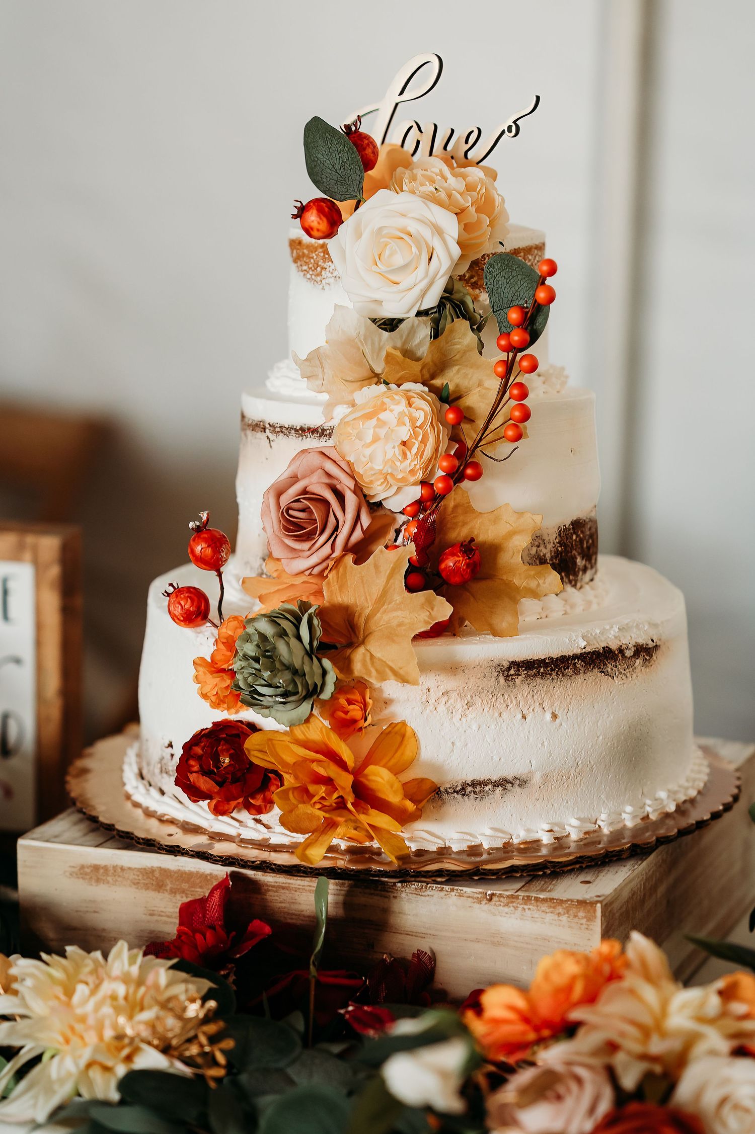 Elegant wedding cake decorated with autumn-colored flowers, succulents, and berries in a rustic semi-naked style.