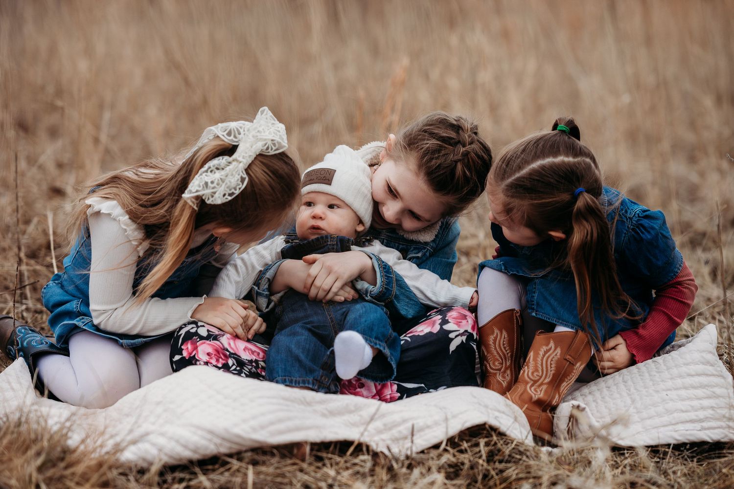 Four young children sitting together on a blanket in a golden field, lovingly gathered around a newborn baby.