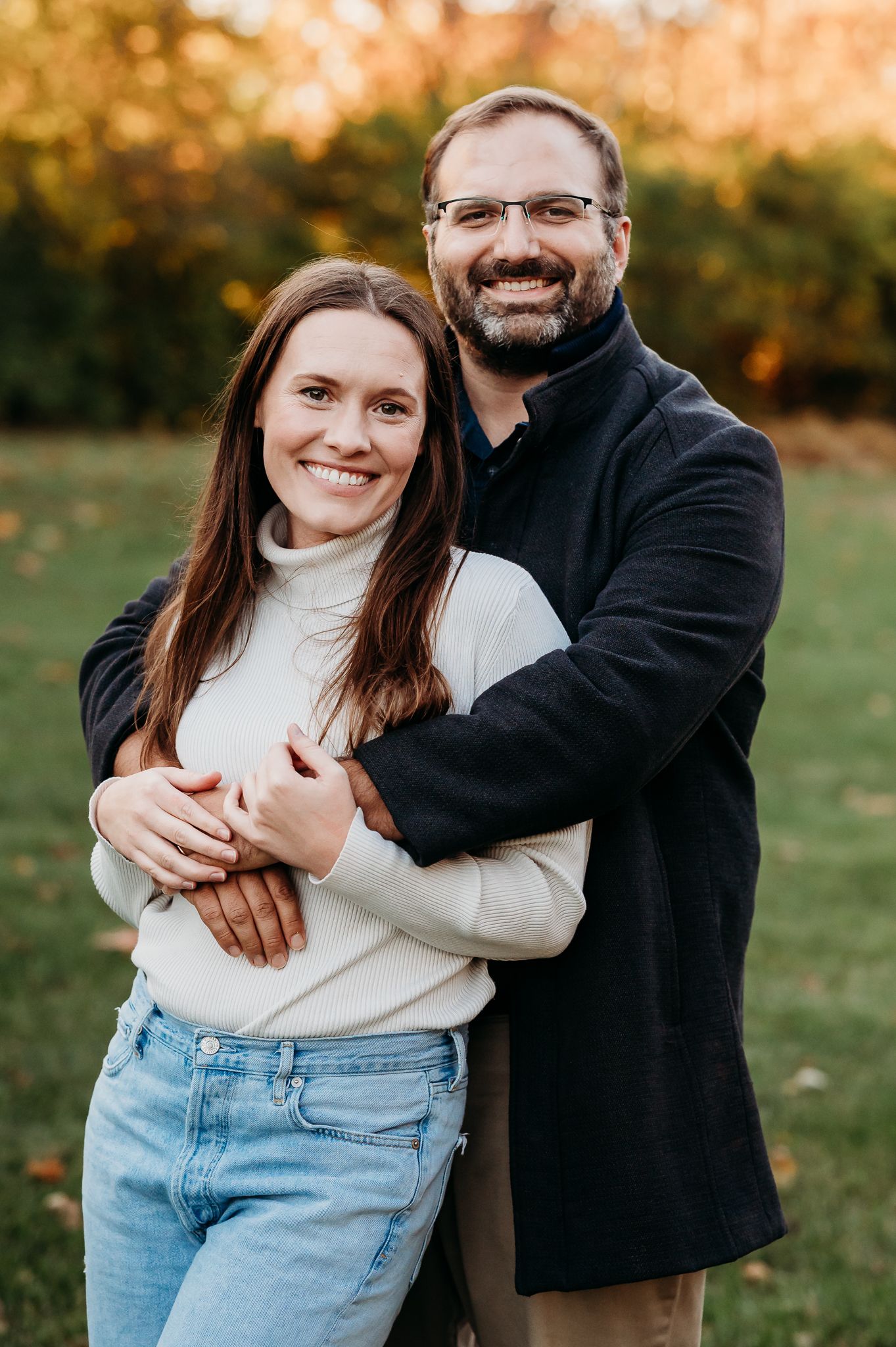 A couple embraces in warm autumn sunlight with fall foliage in the background  at Friendship Gardens in Plainfield.