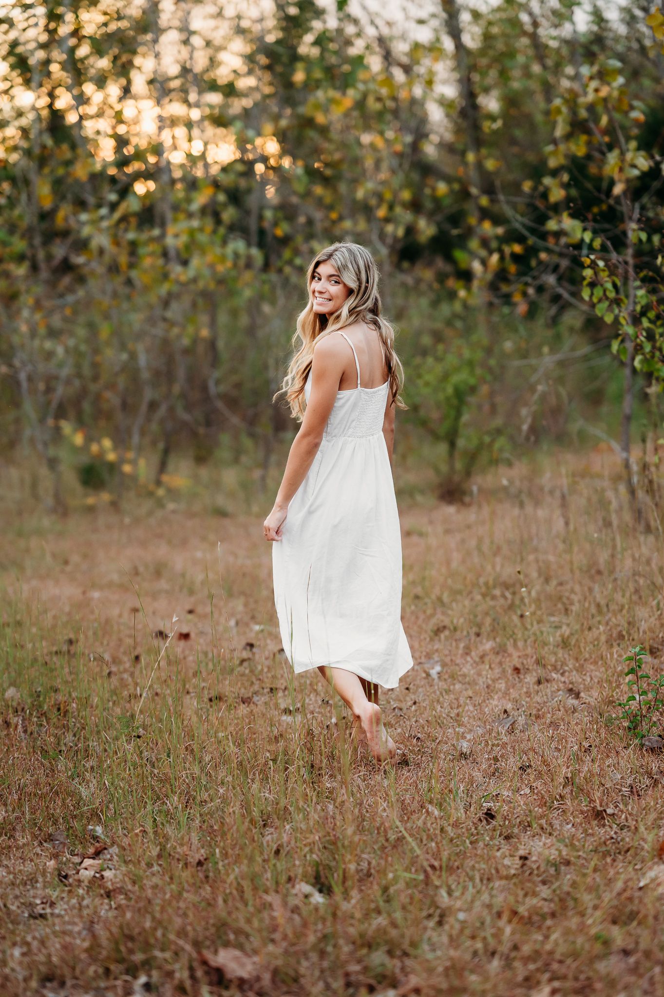 A flowing white sundress catches the late afternoon sunlight in an autumn field with golden bokeh.