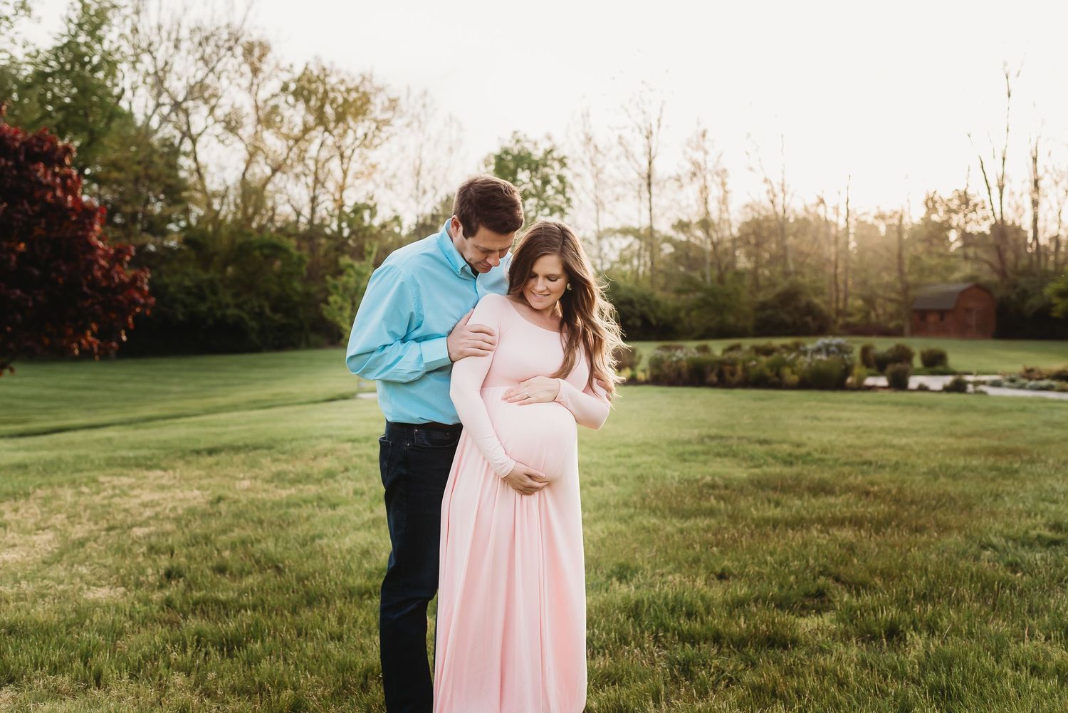 A loving outdoor maternity photoshoot featuring coordinated outfits in pink and blue tones at sunset in Plainfield's Friendship Gardens.