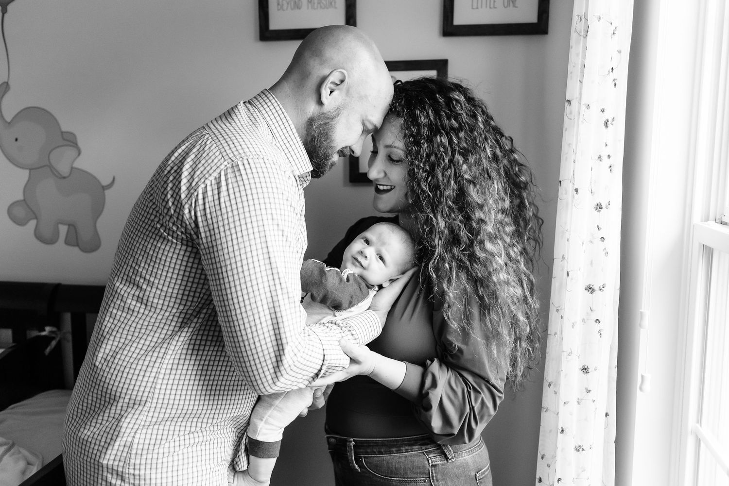 Black and white photo showing tender moment between a couple and their baby boy in Avon, Indiana, home nursery.