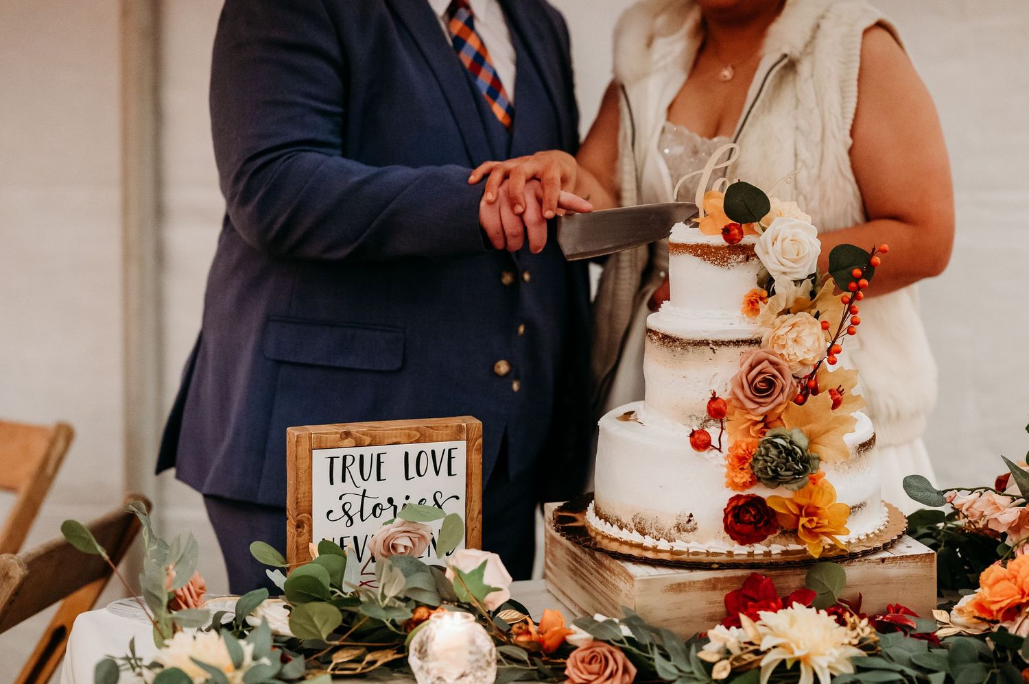 Wedding reception table decorated with autumn colors, cake, and rustic decor against white backdrop.