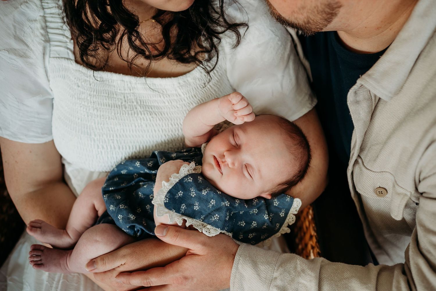 Parents cradling their sleeping newborn baby dressed in a navy floral outfit during an intimate lifestyle newborn photo session.