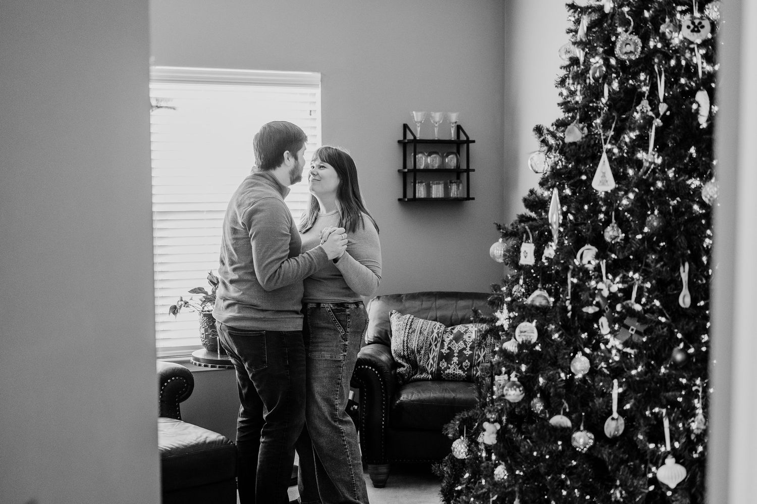 Black and white photo of a couple sharing a romantic moment near a decorated Christmas tree in their Indianapolis home.
