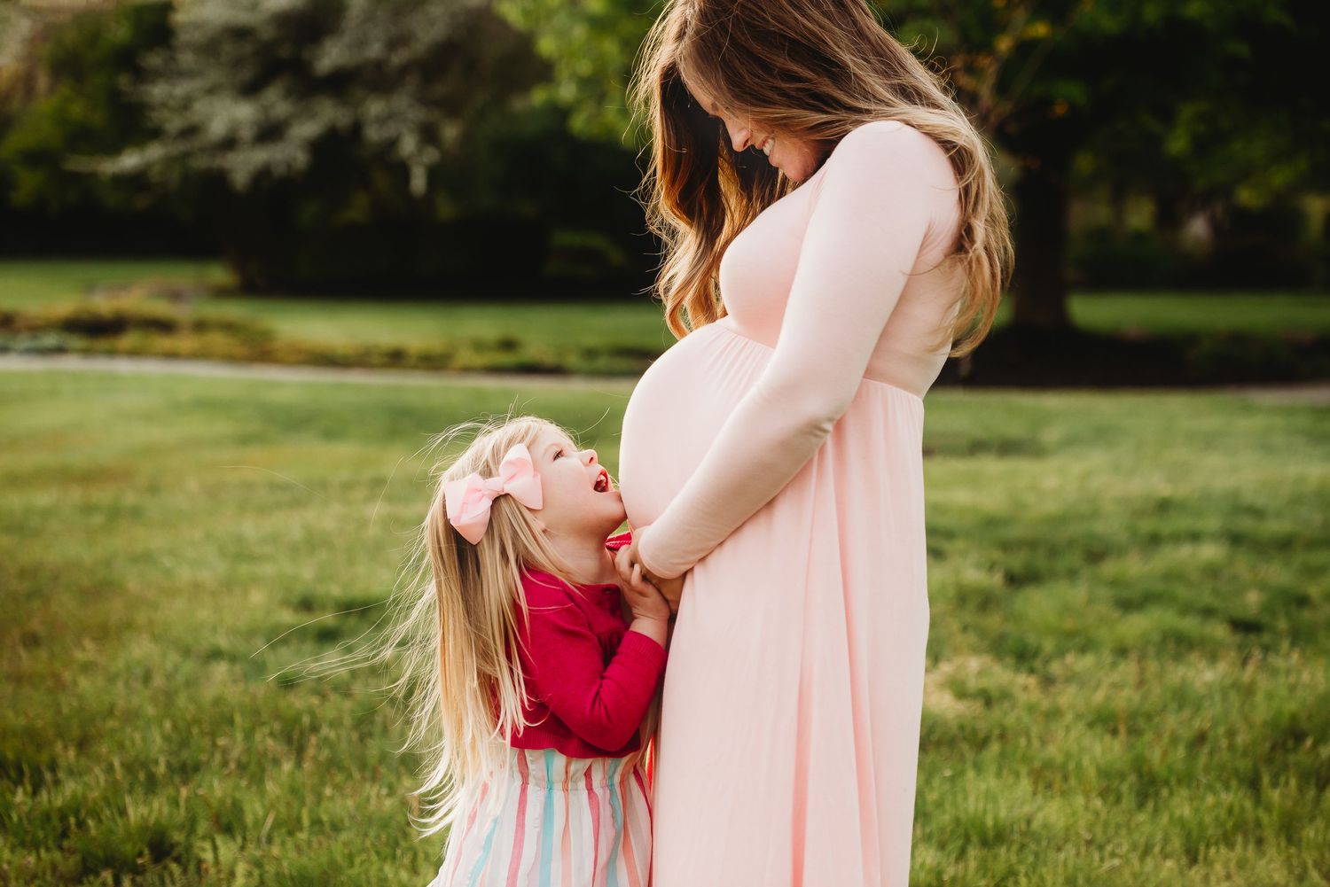 A mom and little girl in pink outfits embrace tenderly during spring maternity photoshoot in Friendship Gardens in Plainfield, Indiana.